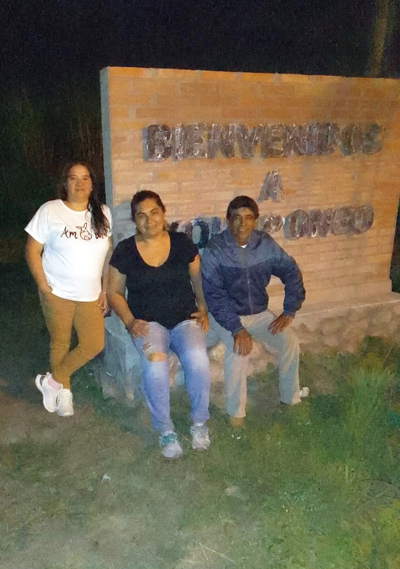 Myriam Cruz, Vilma Gómez, y Tino, del Club 25 de Mayo, sonrientes en el ingreso a Yonopongo, a la vera de la ruta 38: "Pronto van a volver a pintar las letras, pero este es nuestro cartel identificatorio", cuentan