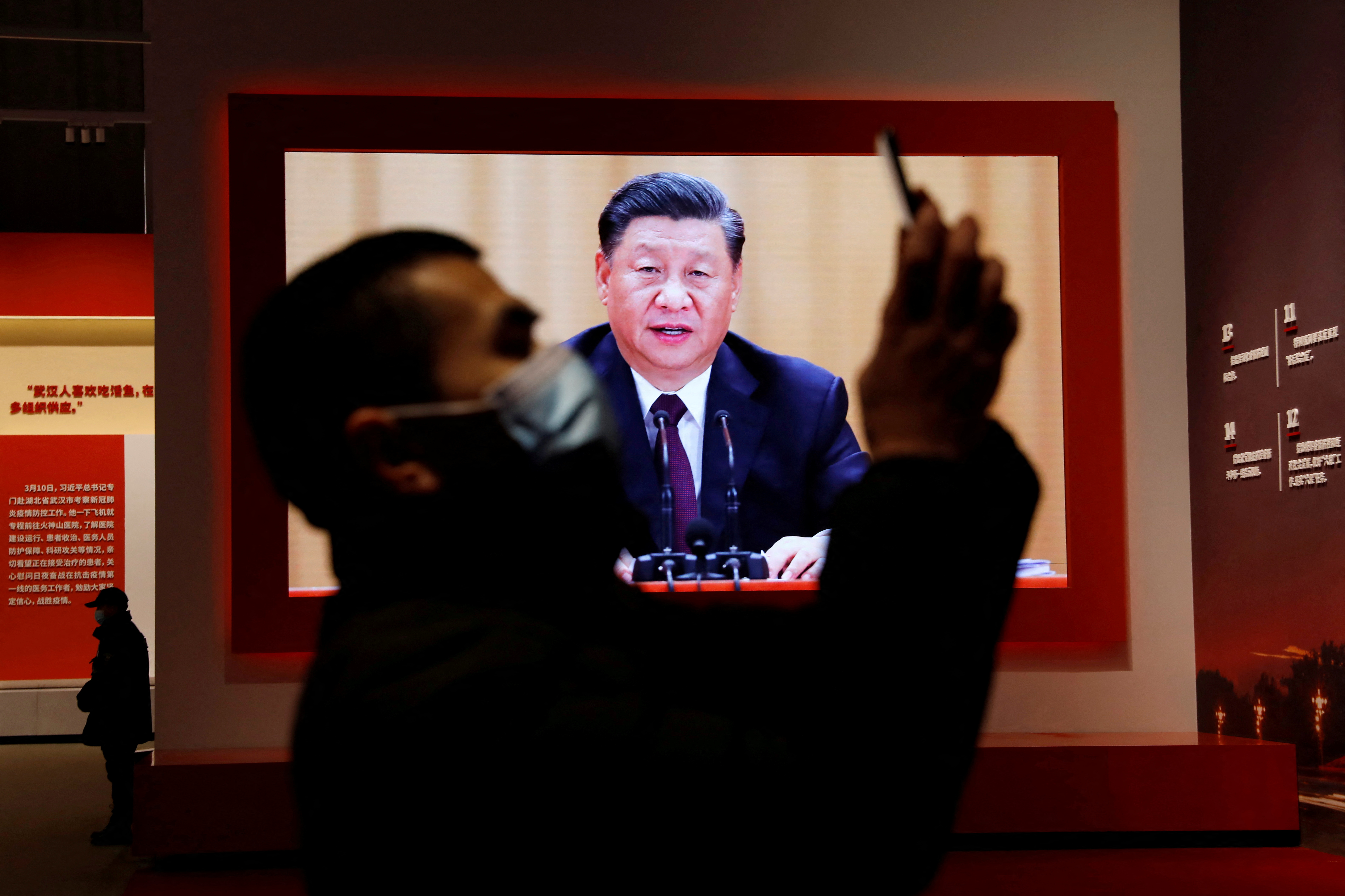 FOTO DE ARCHIVO: Un visitante sostiene su teléfono móvil cerca de una pantalla que muestra al presidente chino Xi Jinping durante una exposición sobre la lucha contra el COVID-19, cuya política de Covid Cero está golpeando nuevamente la economía de China (Reuters)