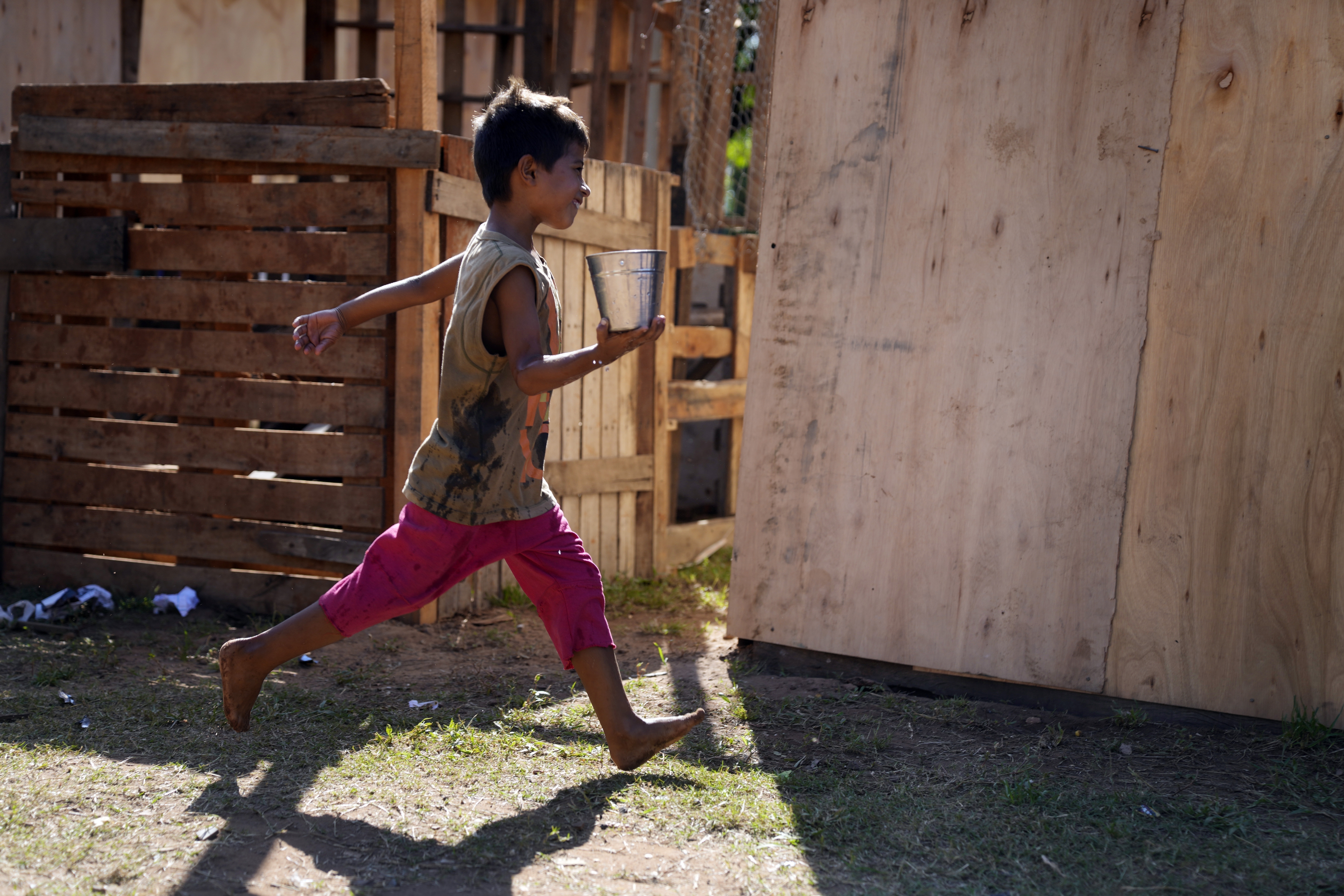 Un niño, desplazado por las crecidas del Río Paraguay, corre con un recipiente lleno de agua en una mano, en su refugio temporal en Asunción, Paraguay, el 18 de marzo de 2023. (AP Foto/Jorge Saenz)