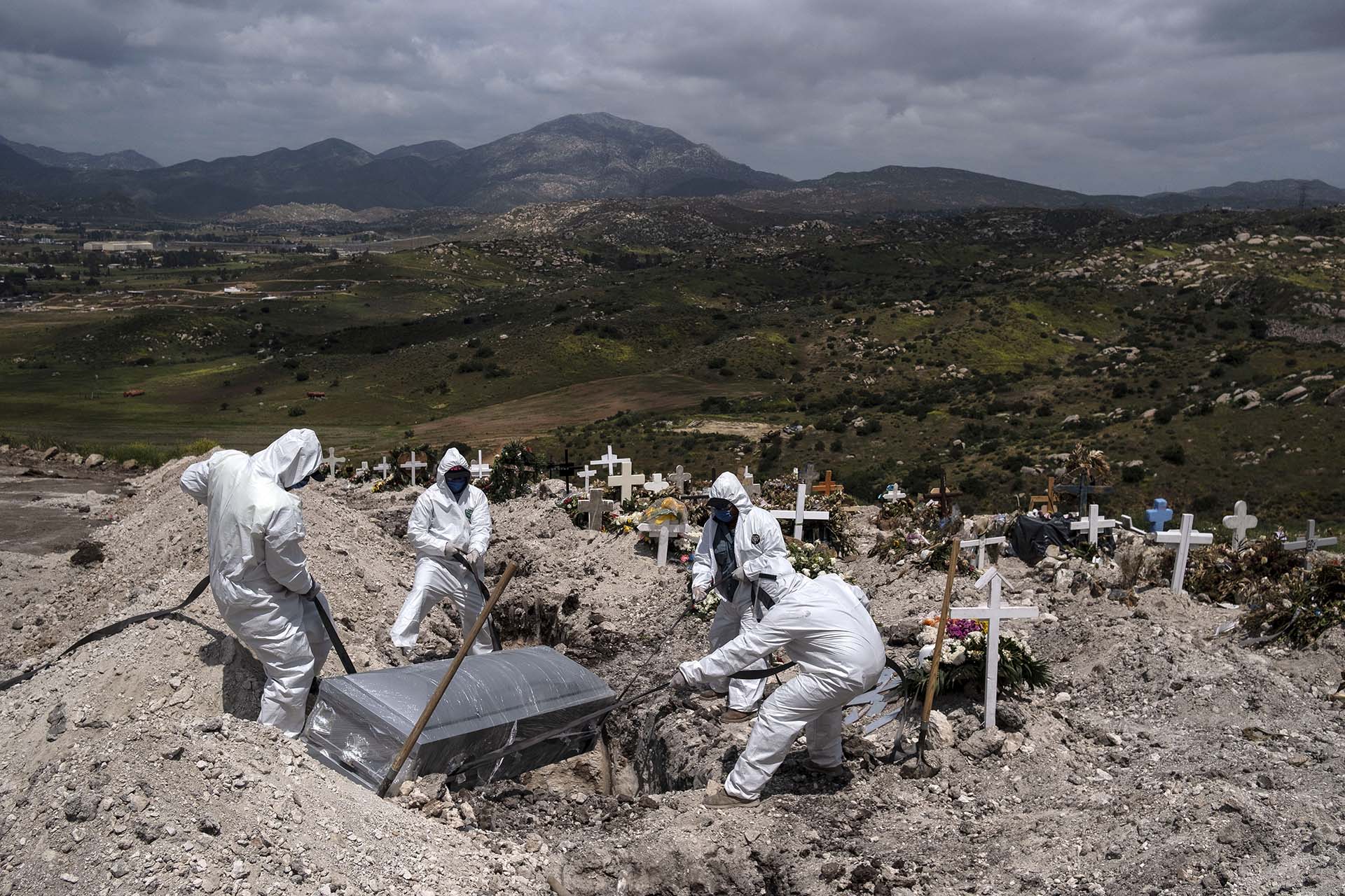 Trabajadores con trajes especiales sepultan el cuerpo de una víctima de covid-19 que nadie reclamó en el cementerio municipal de Tijuana, México (21 de abril) 