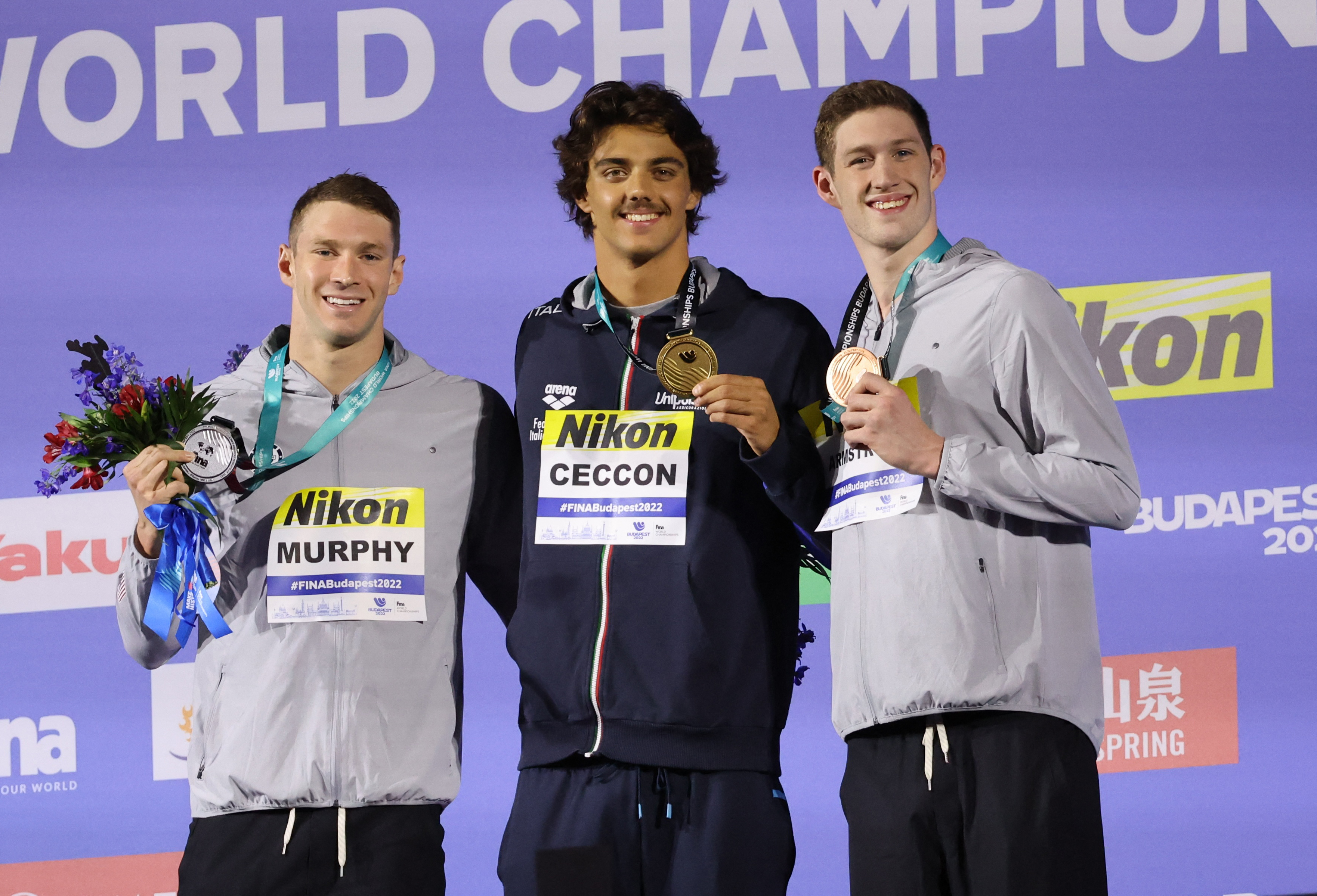 Swimming - FINA World Championships - Budapest, Hungary - June 20, 2022 Gold medallist Italy's Thomas Ceccon celebrates on the podium after winning the men's 100m backstroke final with silver medallist Ryan Murphy of the U.S. and bronze medallist Hunter Armstrong of the U.S. REUTERS/Antonio Bronic