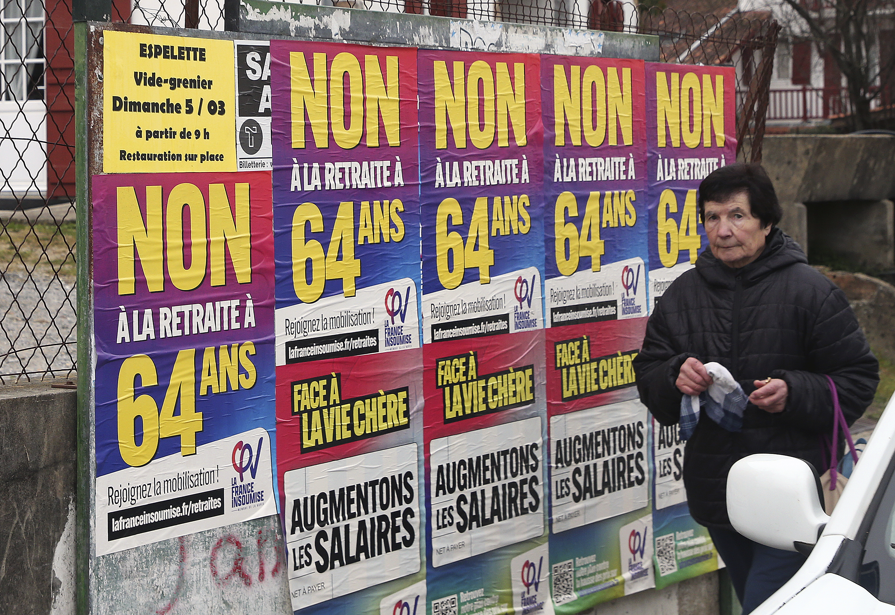 Una mujer pasa junto a carteles que dicen "No a la jubilación a los 64" en Saint Pee sur Nivelle, en el suroeste de Francia, el lunes 6 de marzo de 2023. Los sindicatos amenazaban con paralizar la economía francesa esta semana, en lo que esperaban fuera su mayor desafío al plan del presidente, Emmanuel Macron, de subir la edad de jubilación. (AP Foto Bob Edme)