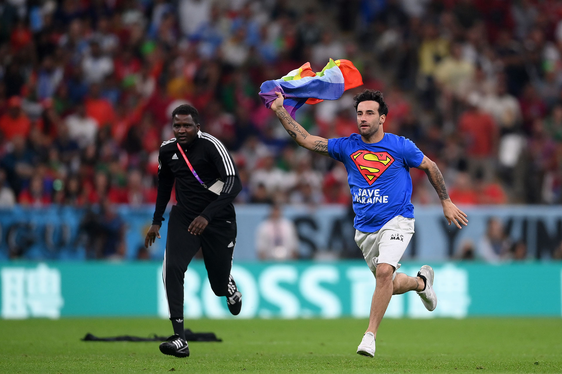 Un espectador con una remera con la frase "Salven a Ucrania" y una bandera con los colores de la comunidad LGBT+ invade el campo de juego durante el partido entre Portugal y Uruguay en la fase de grupos del Mundial de Qatar. 