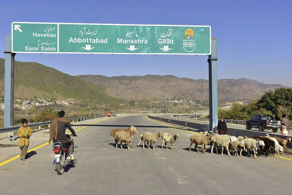 ARCHIVO - Un motociclista pasa junto a ovejas en una carretera recién construida en Haripur, Pakistán, el 22 de diciembre de 2017. China lanzó la Iniciativa de la Franja y la Ruta en 2013 para expandir su comercio e influencia mediante la construcción de carreteras, puertos y otras infraestructuras en el extranjero. (AP Photo/Aqeel Ahmed)