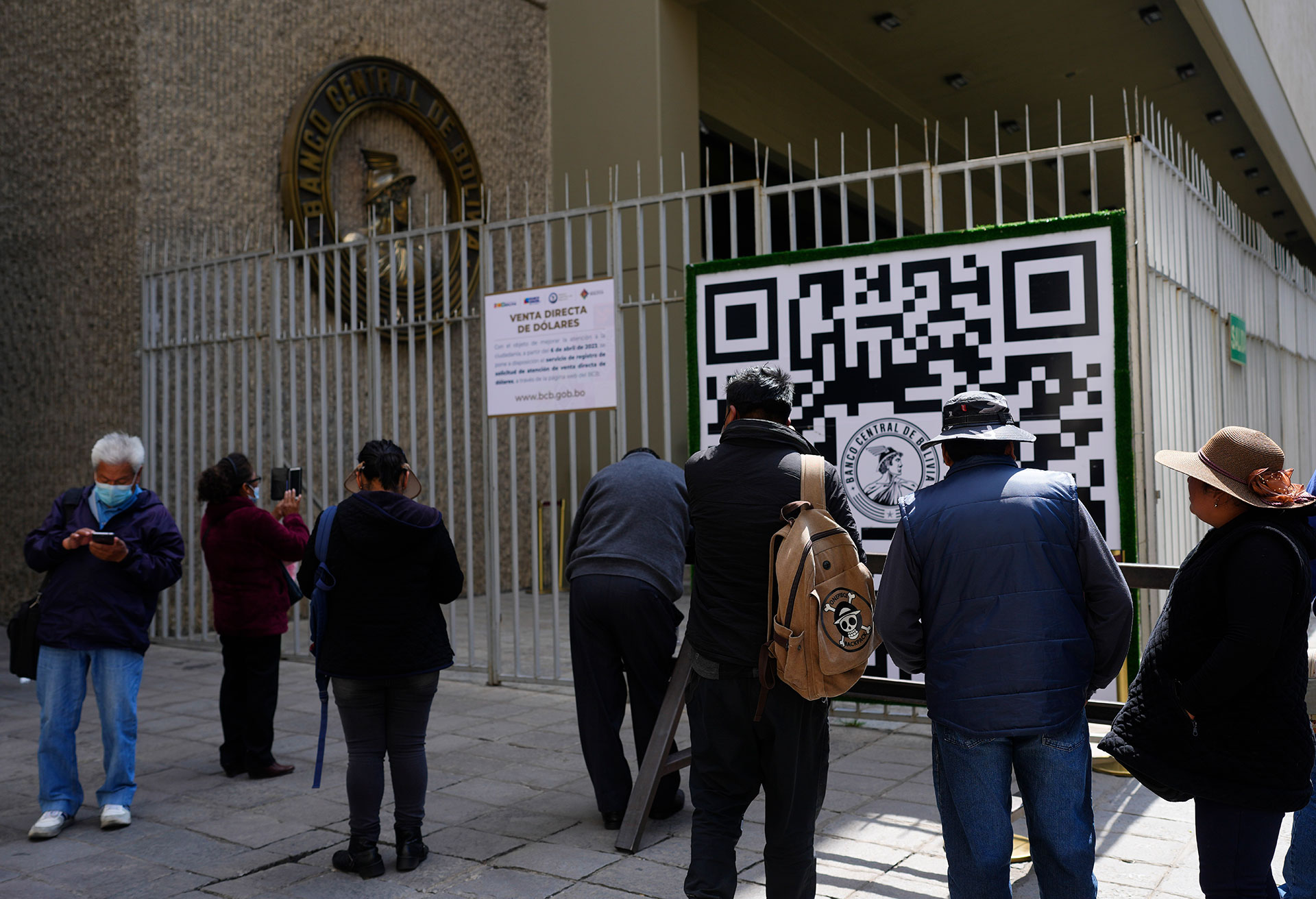 Varias personas miran un código QR afuera del Banco Central de Bolivia que las personas deben usar para registrarse a fin de hacer una cita con el banco que luego le dice al usuario cuántos dólares estadounidenses puede comprar en esa fecha, el martes 11 de abril de 2023 en La Paz, Bolivia. (AP Foto/Juan Karita) (AP)