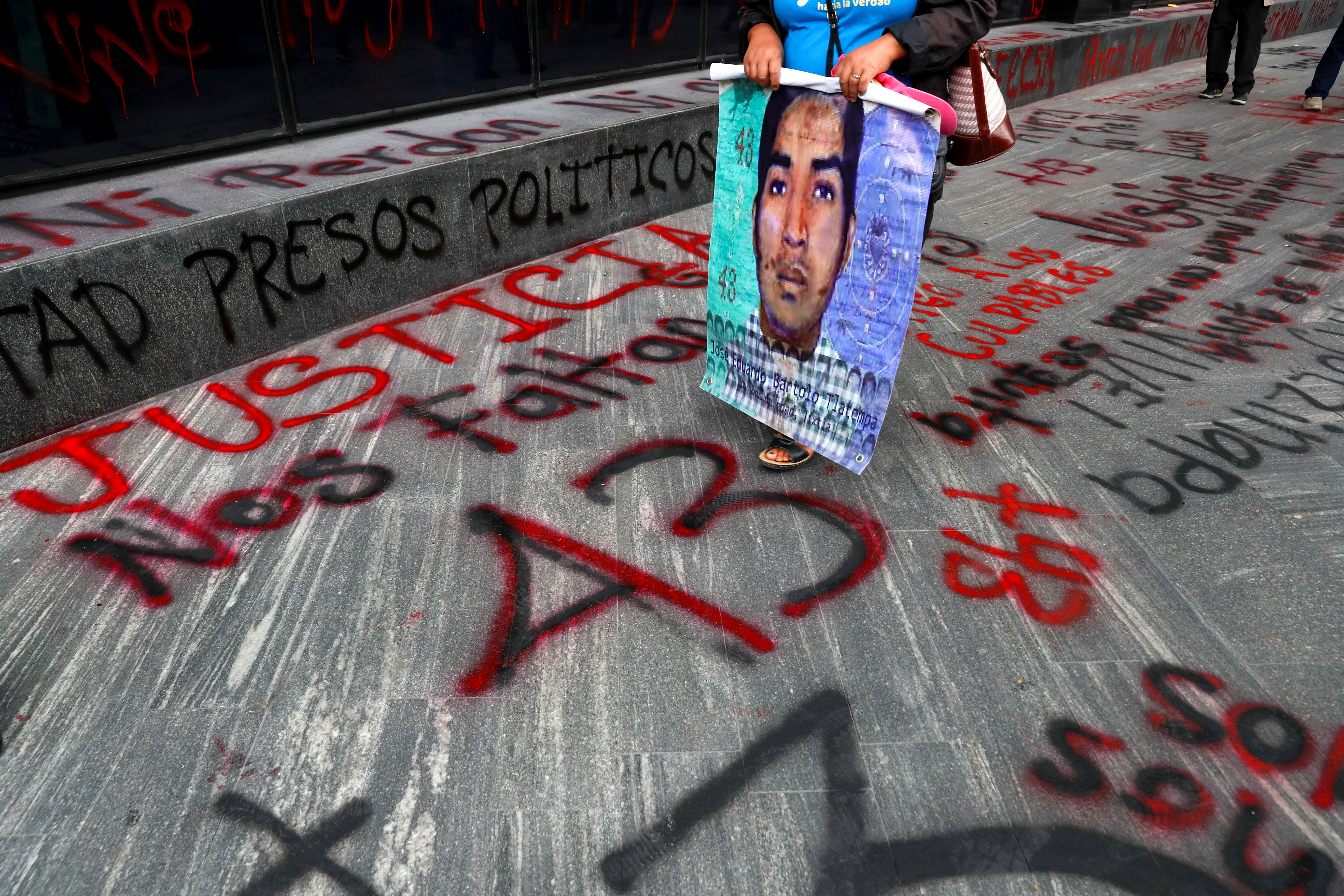 Un familiar de un estudiante desaparecido sostiene un cartel con su imagen mientras pasa junto a un cartel
