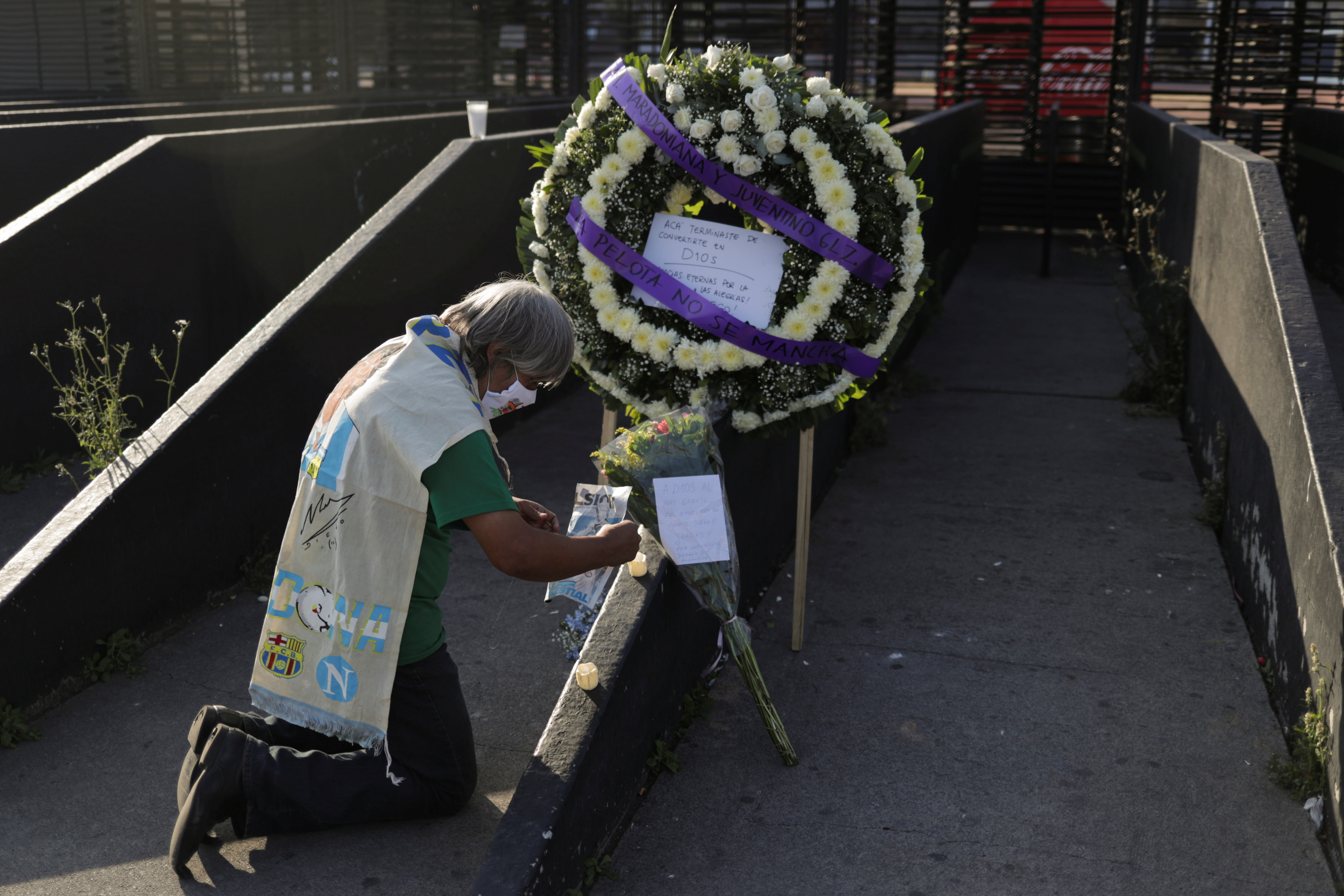 Un fanático se arrodilla mientras coloca una imagen de la leyenda del fútbol argentino Diego Armando Maradona junto a una ofrenda floral en su memoria afuera del estadio Azteca, en la Ciudad de México, México, 26 de noviembre de 2020.