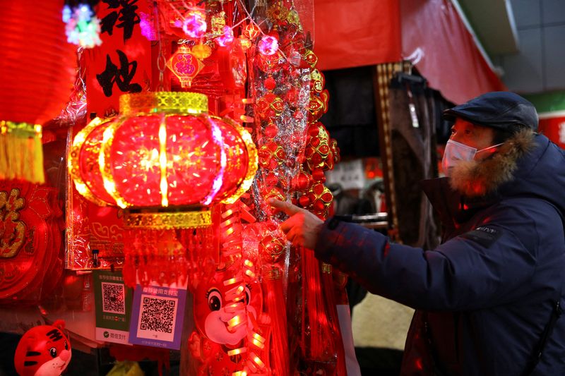 Un hombre con mascarilla observa varios objetos de decoración para la celebración del Año Nuevo Lunar en un puesto de venta en el interior de un mercado de Beijing, China