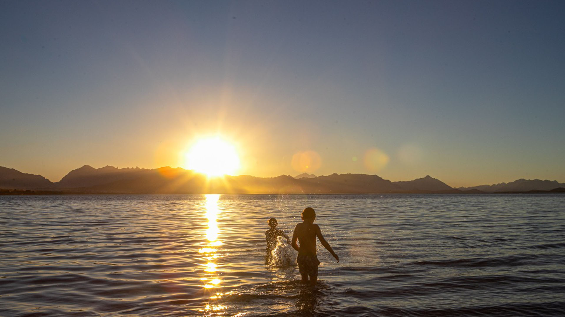Dos niños juegan en las aguas del Nahuel Huapi a la luz del atardecer