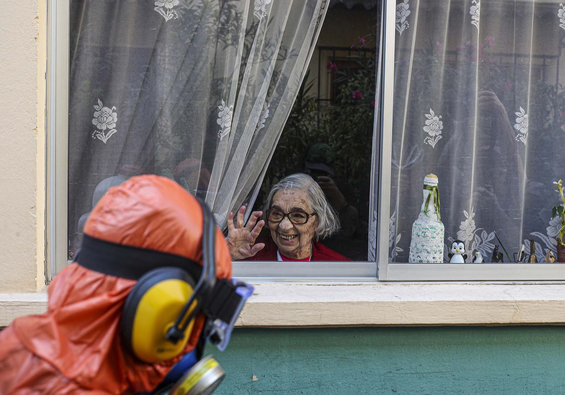 Una mujer saluda y sonríe a un trabajador vestido en un traje especial mientras desinfecta las calles de Santiago, Chile (AP Photo/Esteban Felix)