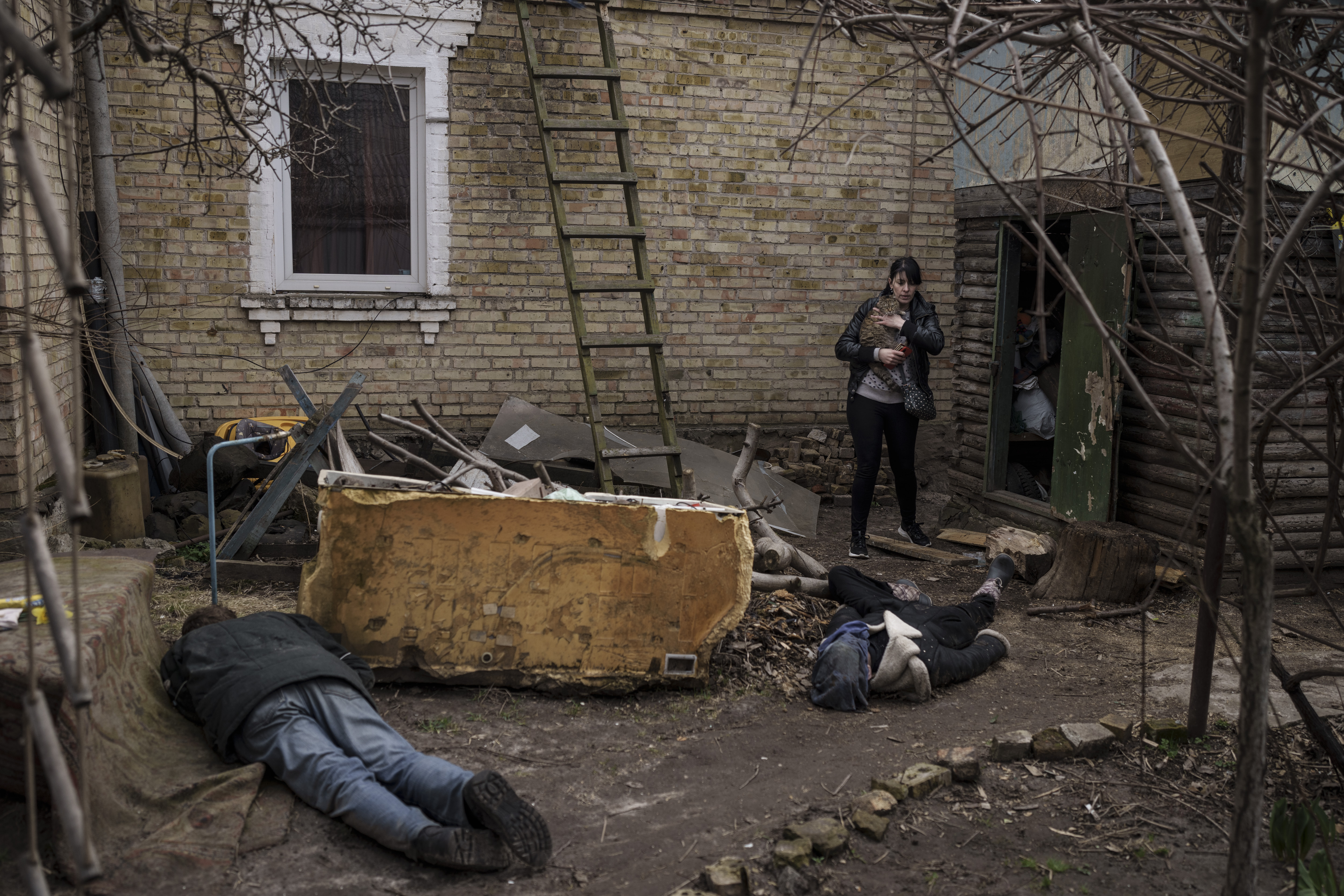 Ira Gavriluk sostiene a su gato mientras camina junto a los cuerpos de su esposo, hermano y otro hombre, que fueron asesinados frente a su casa en Bucha, Ucrania, el lunes 4 de abril de 2022.  (Foto AP/Felipe Dana, archivo)

