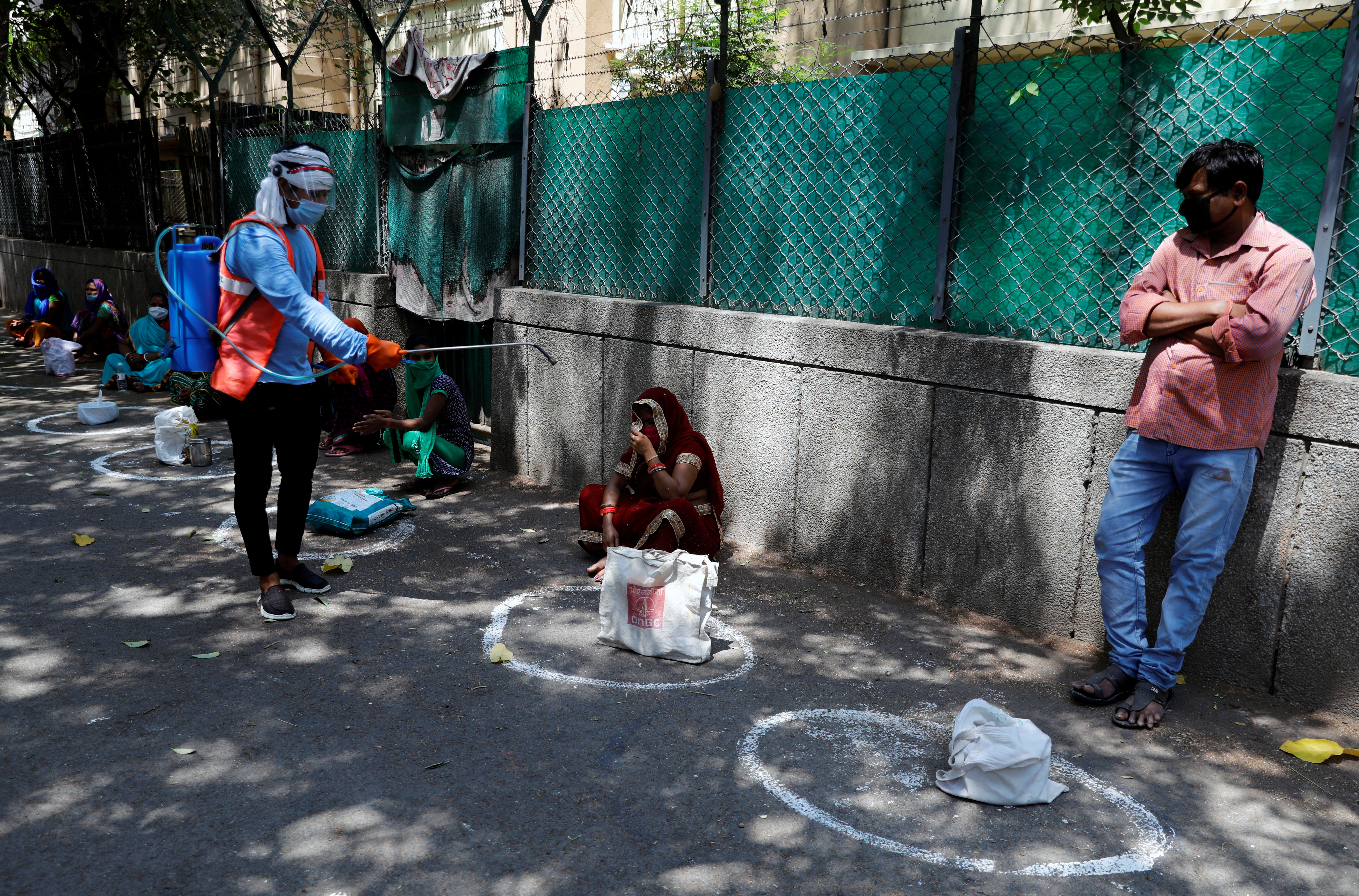 Un trabajador municipal rocía desinfectante en las bolsas de la gente, mientras mantienen el distanciamiento social en una fila para recibir alimentos gratuitos distribuidos por el gobierno en Nueva Delhi, India, el 21 de abril de 2020. REUTERS/Anushree Fadnavis