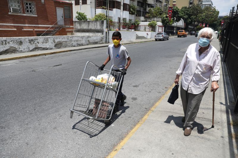 Un niño ayuda a una anciana a llevar compras de alimentos tras la flexibilización de la cuarentena en Caracas.