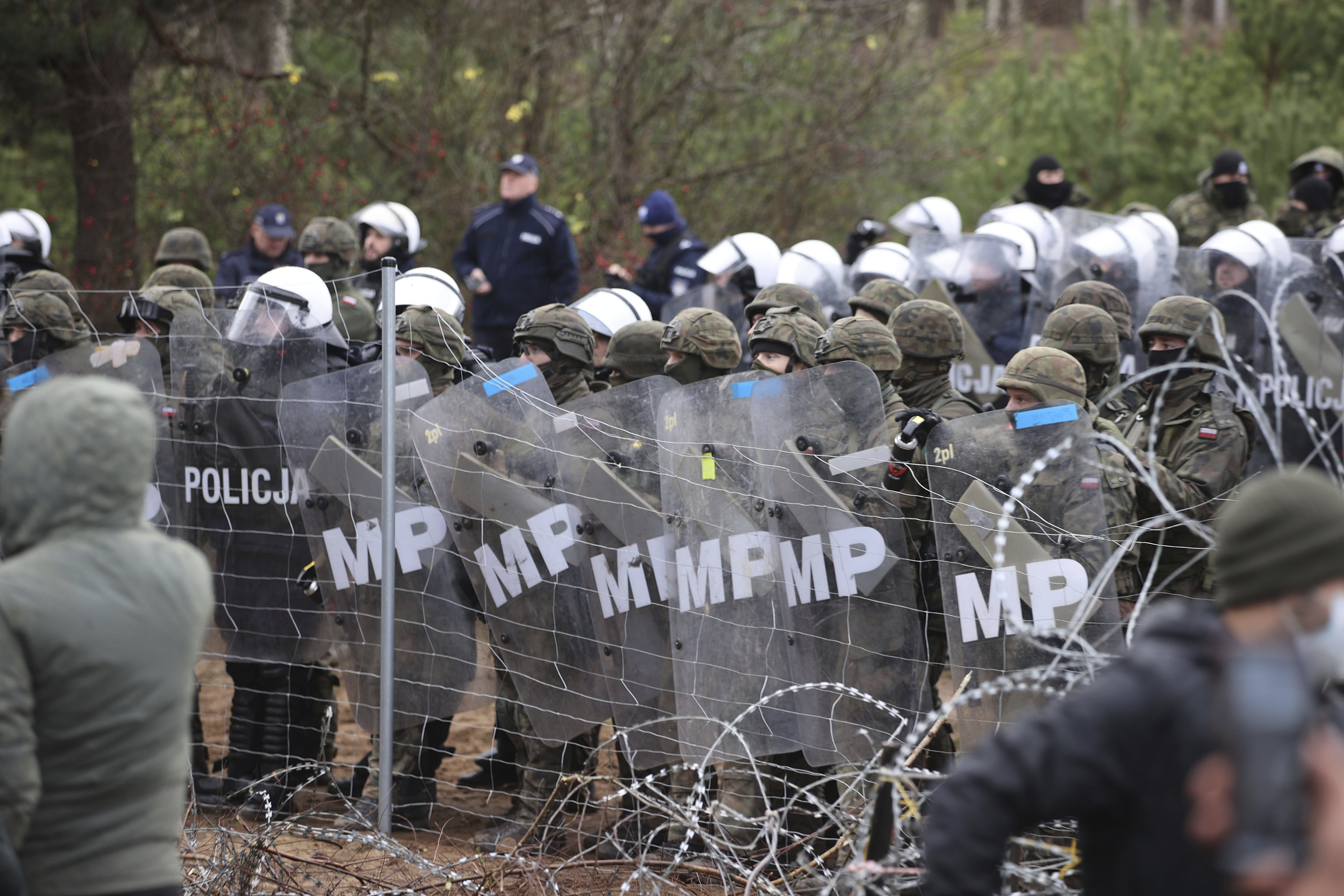 La policía polaca y la policía militar están detrás de la valla fronteriza (Leonid Shcheglov/BelTA via AP)