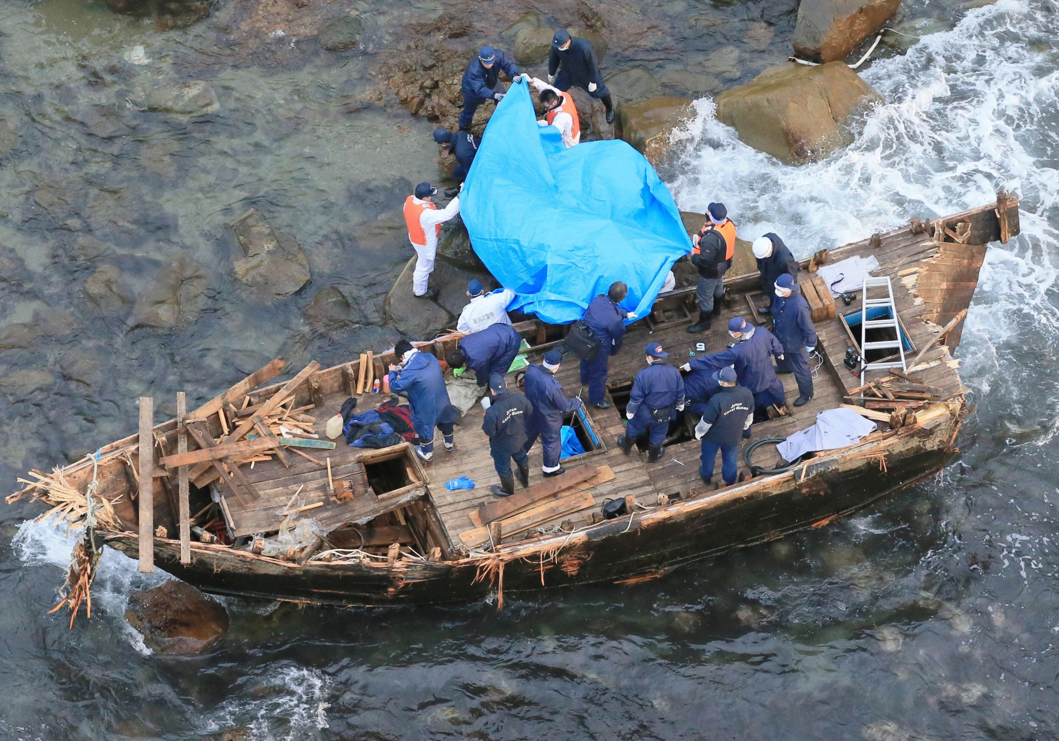 Oficiales de policía japoneses investigan un bote de madera marcado con letras coreanas en la isla de Sado, Japón, el 28 de noviembre de 2012. Se encontraron cinco cuerpos en el bote, que fue arrastrado por las rocas de una playa en la isla. (Kyodo a través de Reuters/archivo)