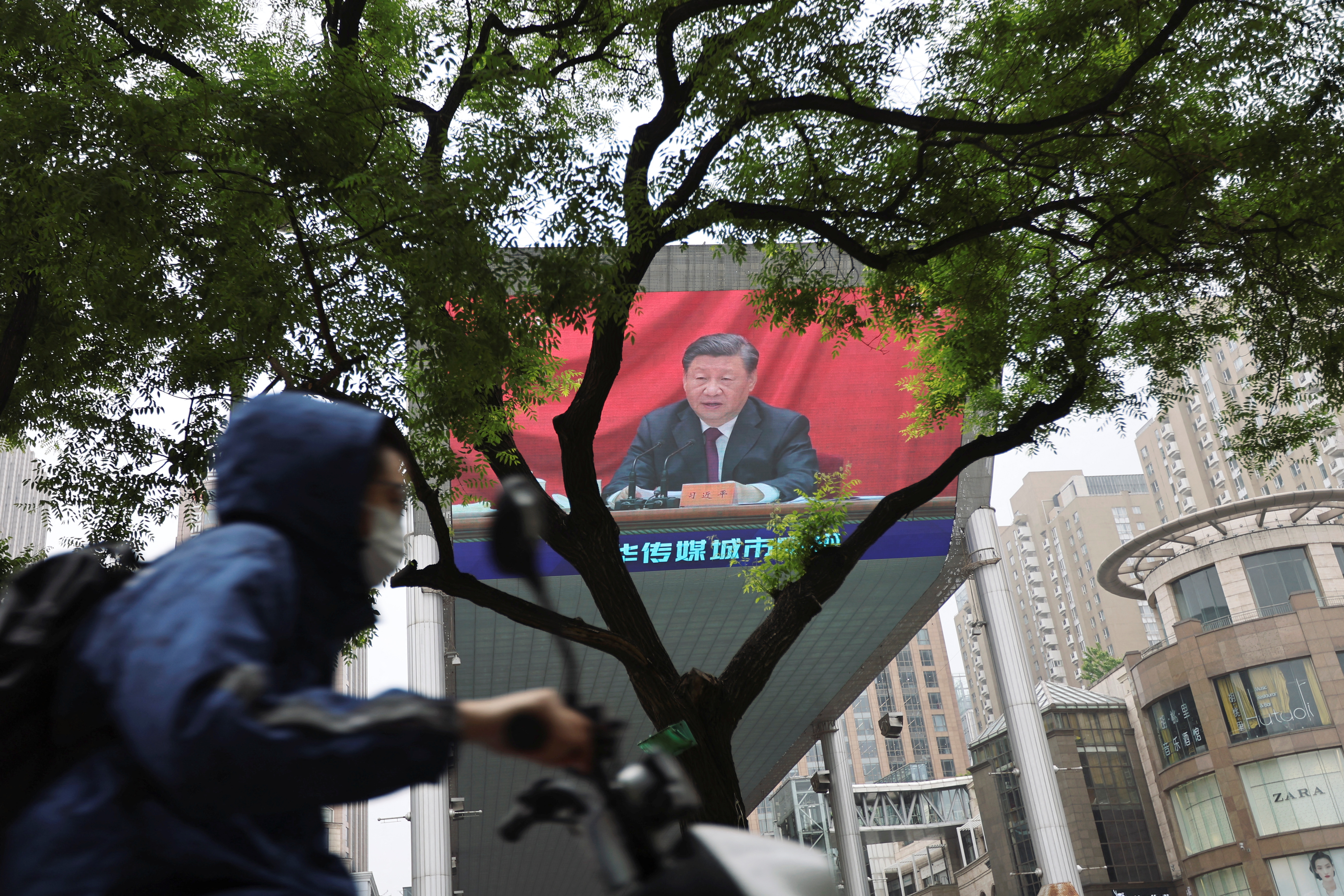 Un hombre con una máscara facial pasa junto a una pantalla gigante que muestra al jefe del régimen chino Xi Jinping hablando en un acto de celebración del centenario de la fundación de la Liga de la Juventud Comunista China, en medio del brote de la enfermedad del coronavirus (COVID-19) en Beijing (Reuters)