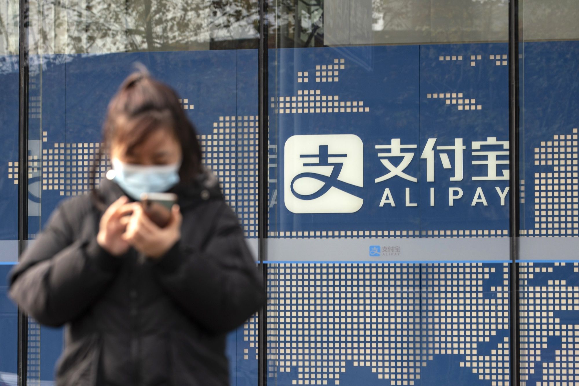 Un peatón utiliza un teléfono inteligente delante de un cartel de Alipay fuera de un edificio de oficinas de Ant Group Co. en Shanghai, China. (AP)