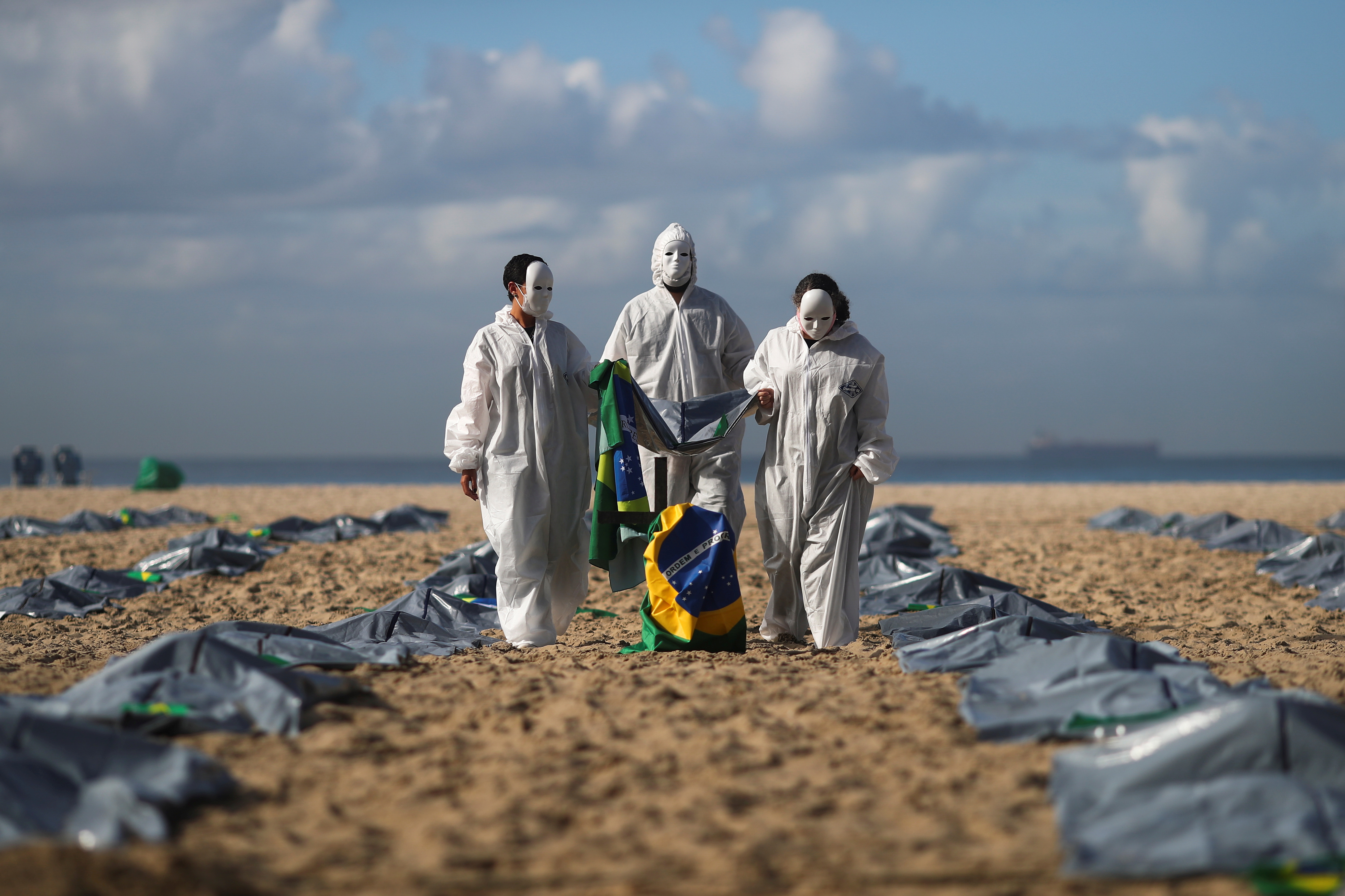 Activistas de la ONG Río de Paz llevan una bandera brasileña mientras muestran cientos de bolsas de plástico, que representan cadáveres, durante una protesta contra las políticas de Jair Bolsonaro, en medio del brote de la enfermedad del coronavirus (COVID-19), en la playa de Copacabana, en Río de Janeiro, Brasil,