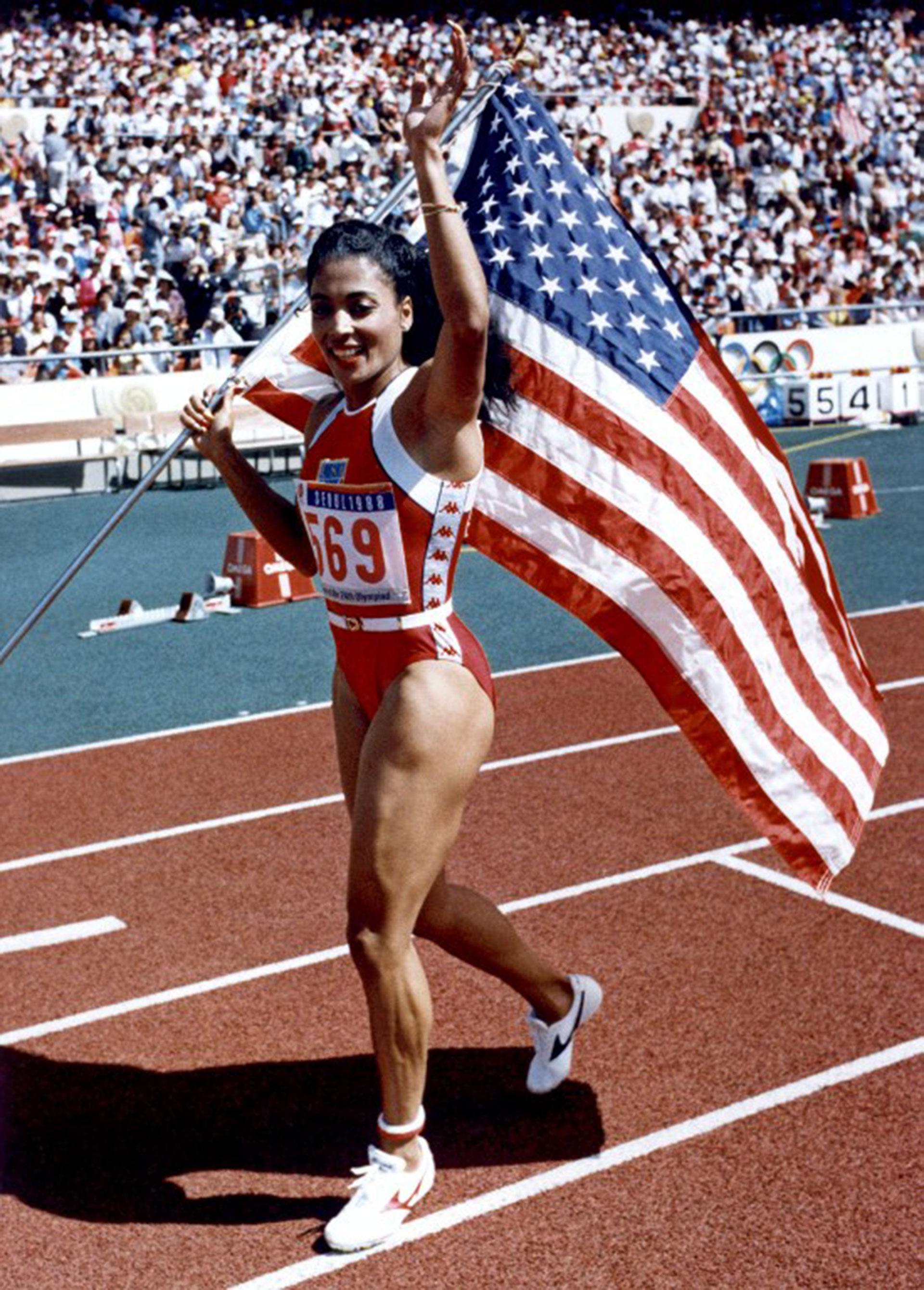 The American Florence Griffith Joyner waves at the crowd as the carries the American flag after setting a new Olympic record and winning the gold for her 10.54 performance at the 100 meters race of Seoul Olympic Games. The American Evelyn Ashford won the silver medal and the German Heike Drechsler won the bronze.(FILM)  AFP PHOTO / AFP PHOTO / IOPP / RON KUNTZ