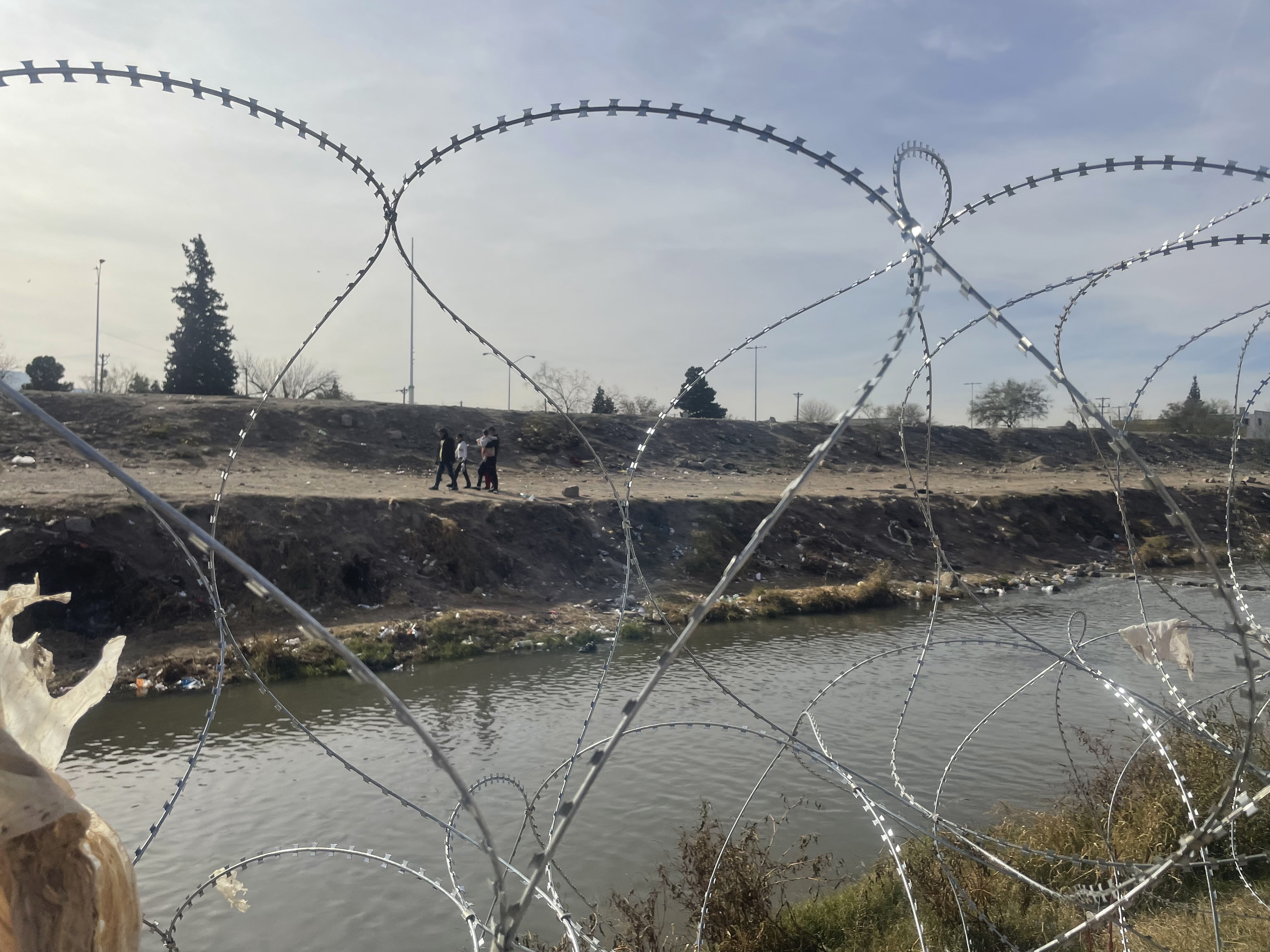 A family is seen on the Mexican side of the Rio Grande River through the concertina wire placed earlier in the day by Texas National Guard troops at site of the recent mass migrant crossings in El Paso, Texas, Tuesday, Dec. 20, 2022. (AP Photo/Giovanna Dell'Orto)