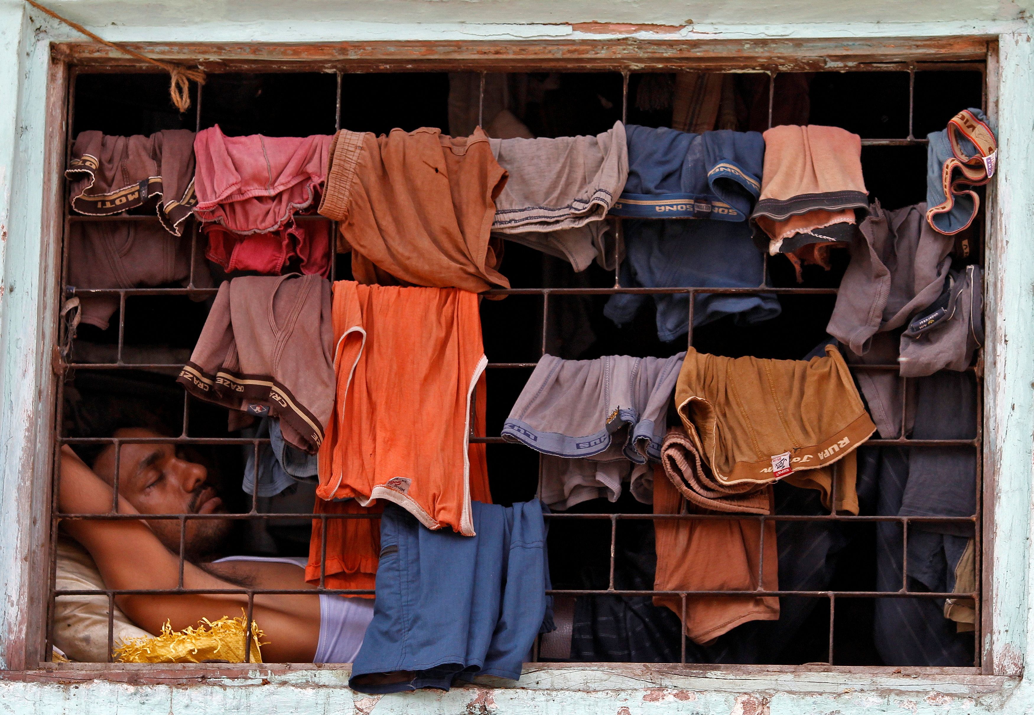 Un habitante de un barrio marginal duerme junto a una ventana con ropa colgada para que se seque, en una chabola de Dharavi, uno de los mayores barrios marginales de Asia, en Bombay el 23 de marzo de 2011.