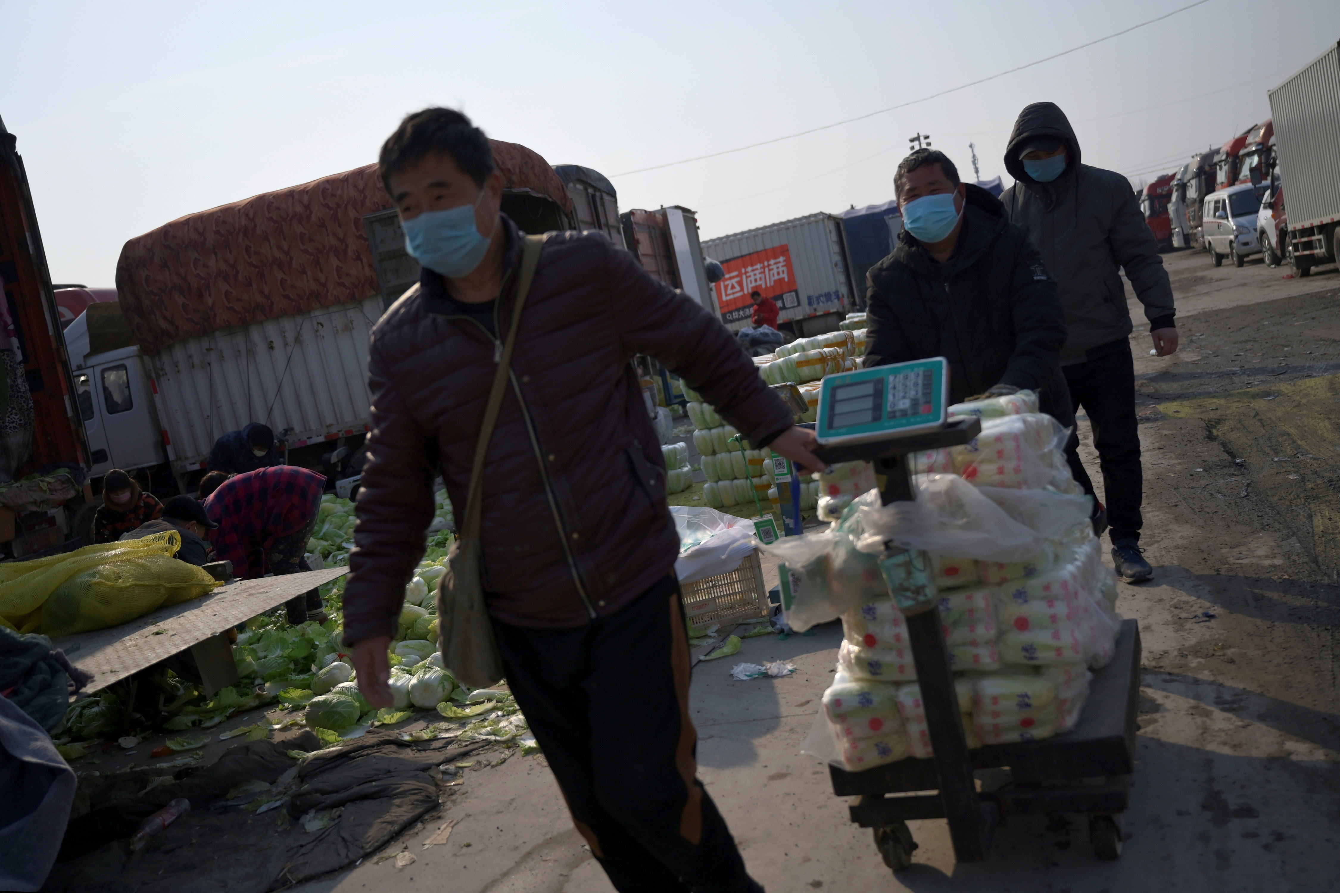 Hombres con máscaras faciales tiran de un carrito que lleva verduras en el mercado mayorista de Xinfadi (Reuters)