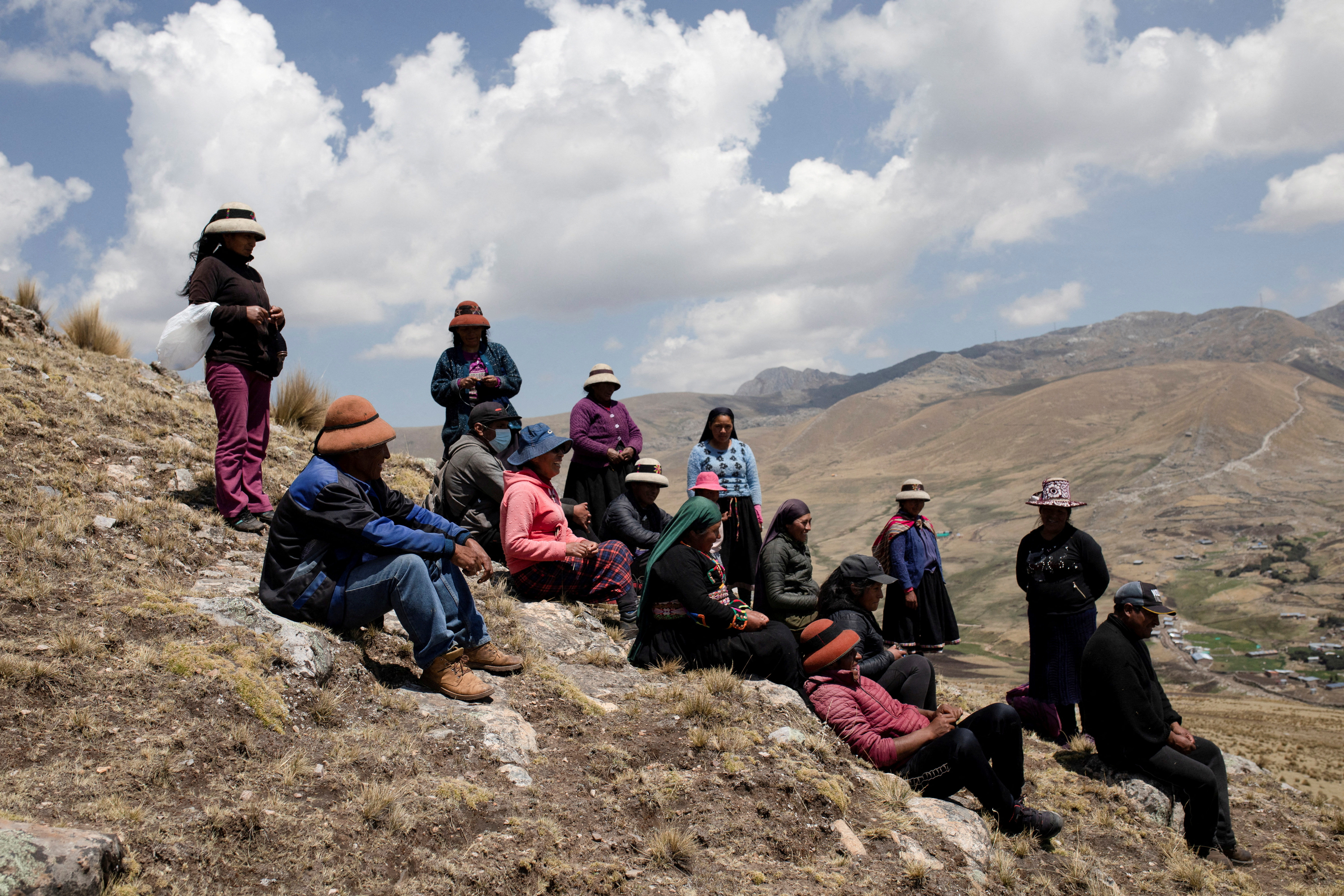 FILE PHOTO: People sit in the mountains in front of a mine operated by MMG Las Bambas, in a region where locals claim mining activity has negatively affected crop yields and killed livestock, outside of Cusco, Peru October 14, 2021. Picture taken October 14, 2021. REUTERS/Angela Ponce/File Photo