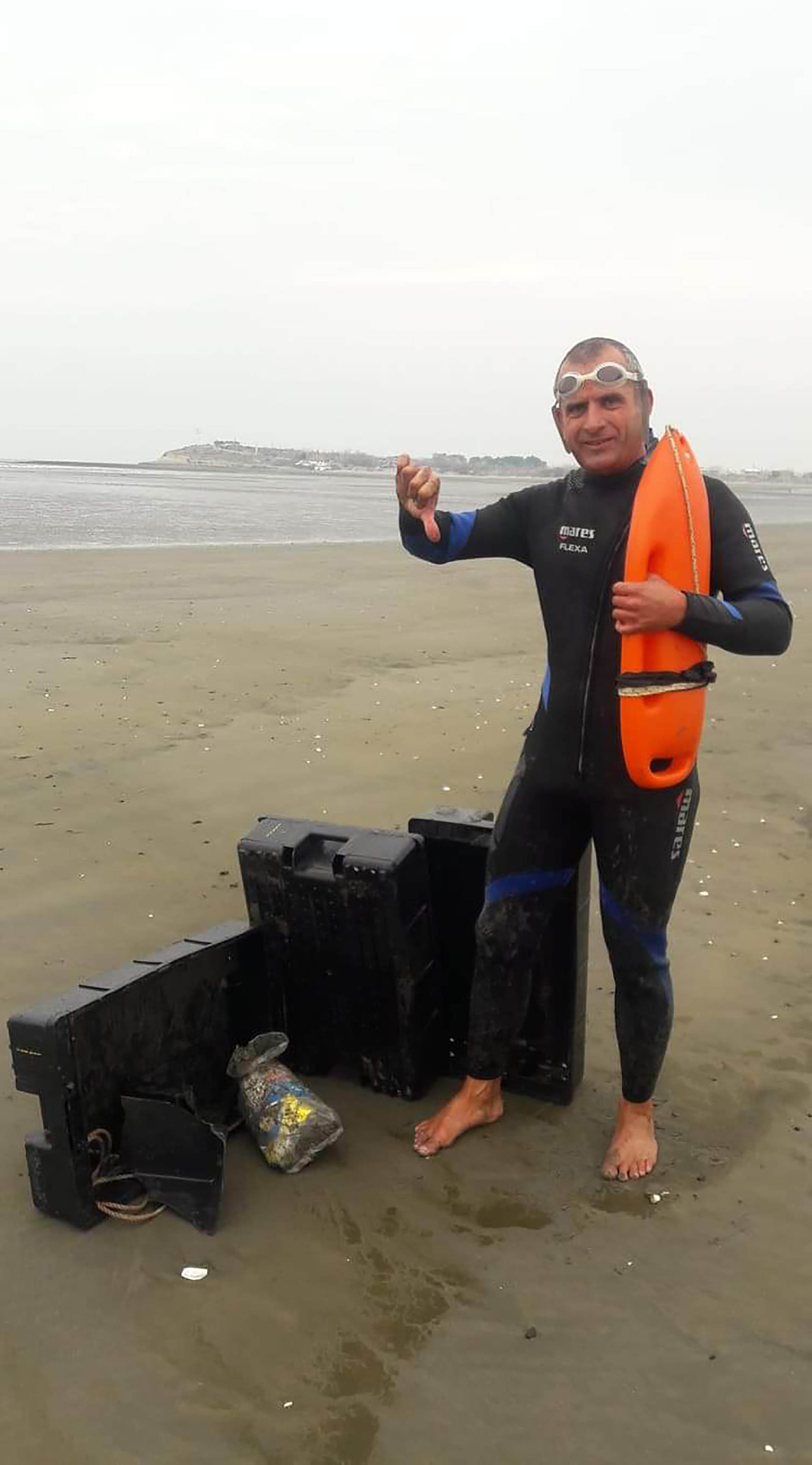 El nadador junto a unos cajones de plástico de la industria pesquera que llegan como basura a las costas de Madryn