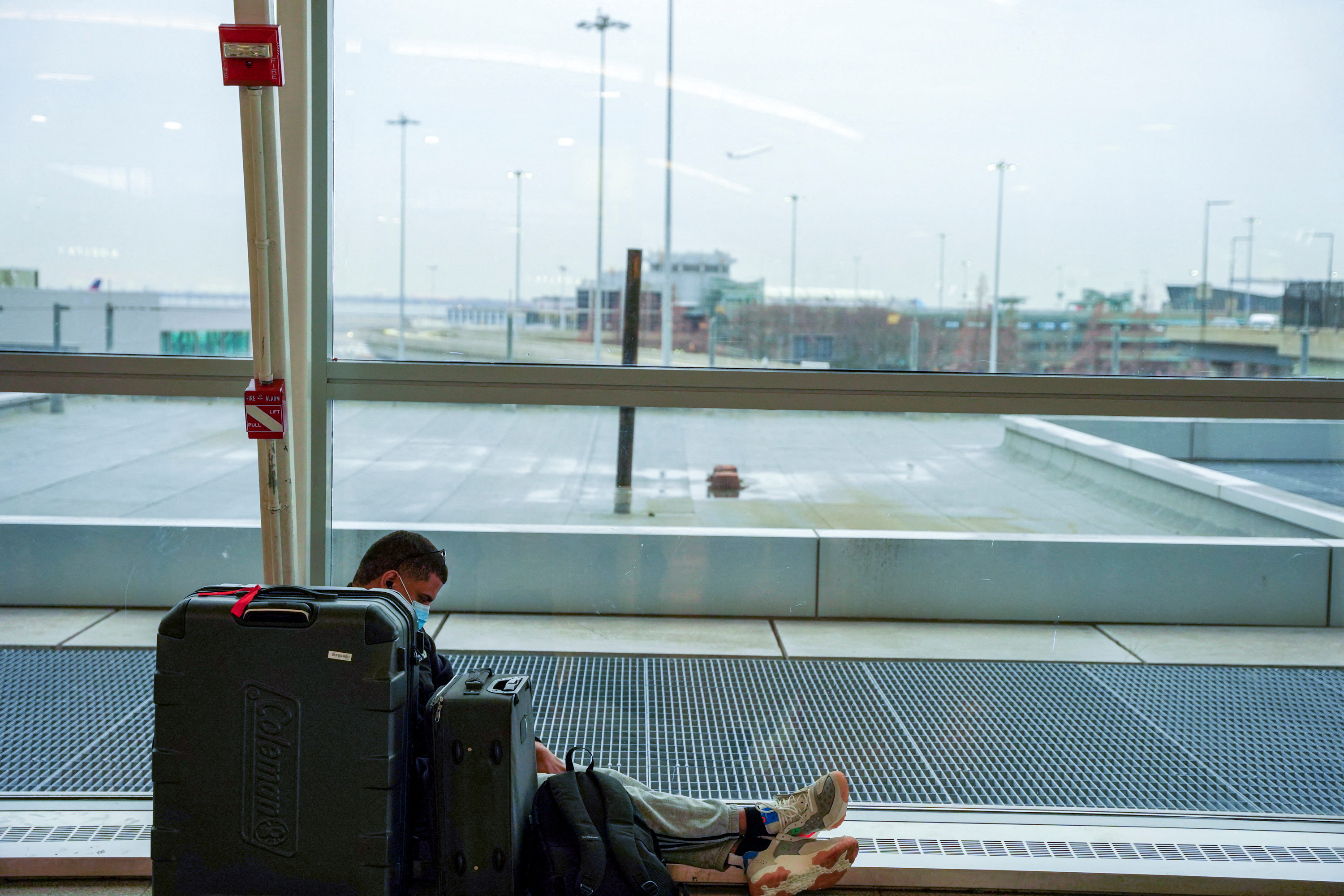 Un pasajero se sienta con su equipaje en el aeropuerto internacional John F. Kennedy después de que las aerolíneas anunciaran la cancelación de numerosos vuelos (Reuters)