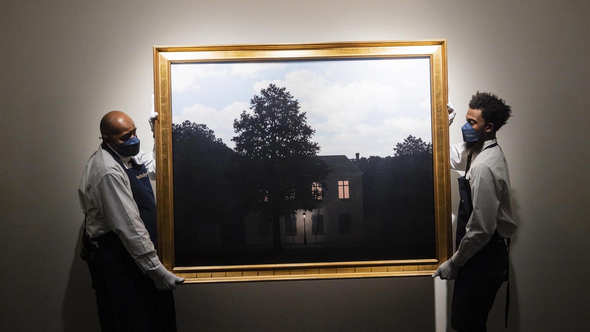 Fotografía de archivo fechada el 21 de enero de 2022, donde aparecen dos empleados de Sotheby's mientras cuelgan la obra "L'empire des lumières", de Rene Magritte, durante una vista previa en la casa de subastas en Nueva York (EFE/ EPA/ Justin Lane)