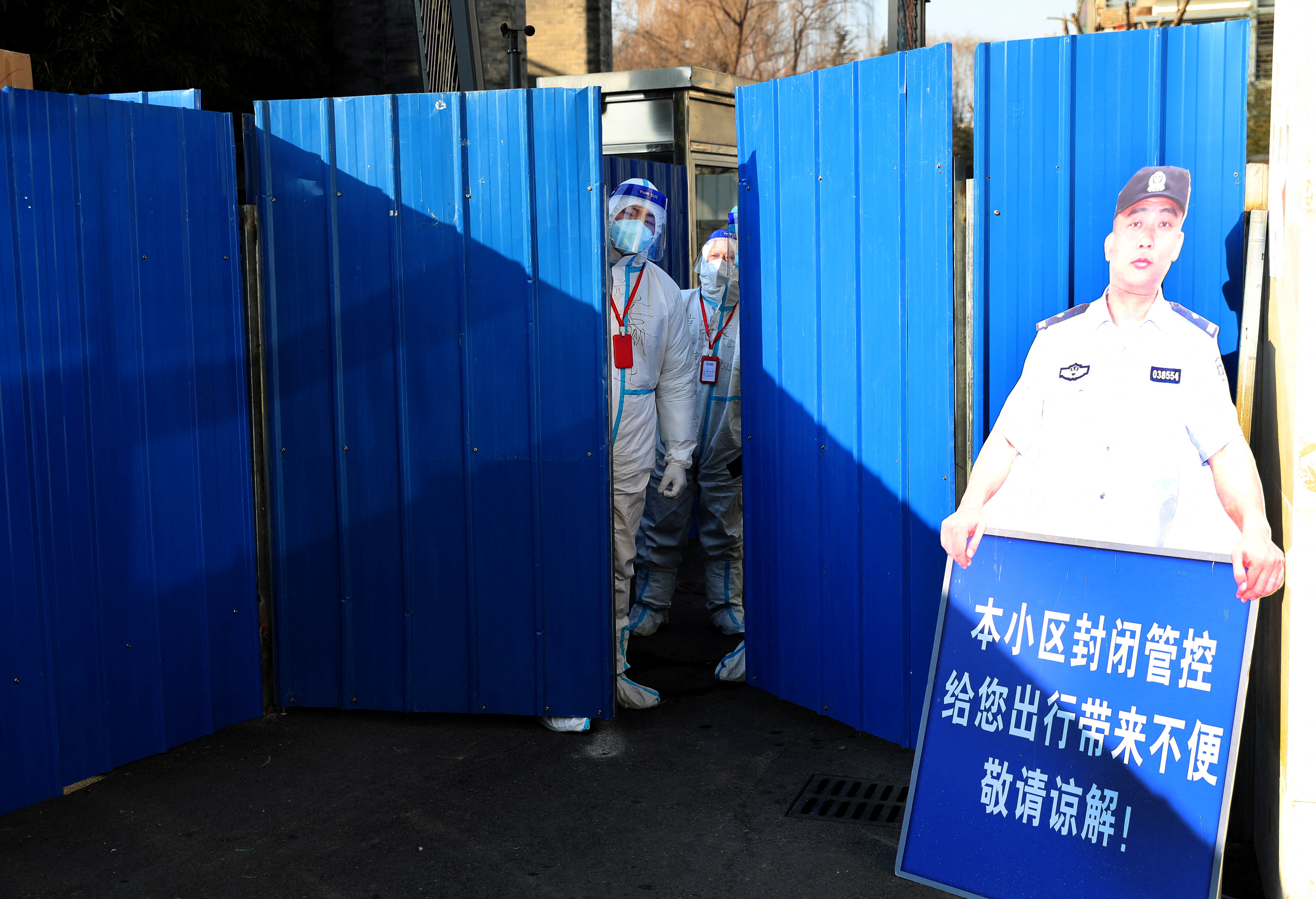 Workers wearing protective suits following the coronavirus disease (COVID-19) outbreak stand at an entrance to a residential compound under lockdown after a case of the Omicron variant was detected, in Beijing's Haidian district, China January 18, 2022. Picture taken January 18, 2022. China Daily via REUTERS  ATTENTION EDITORS - THIS IMAGE WAS PROVIDED BY A THIRD PARTY. CHINA OUT.