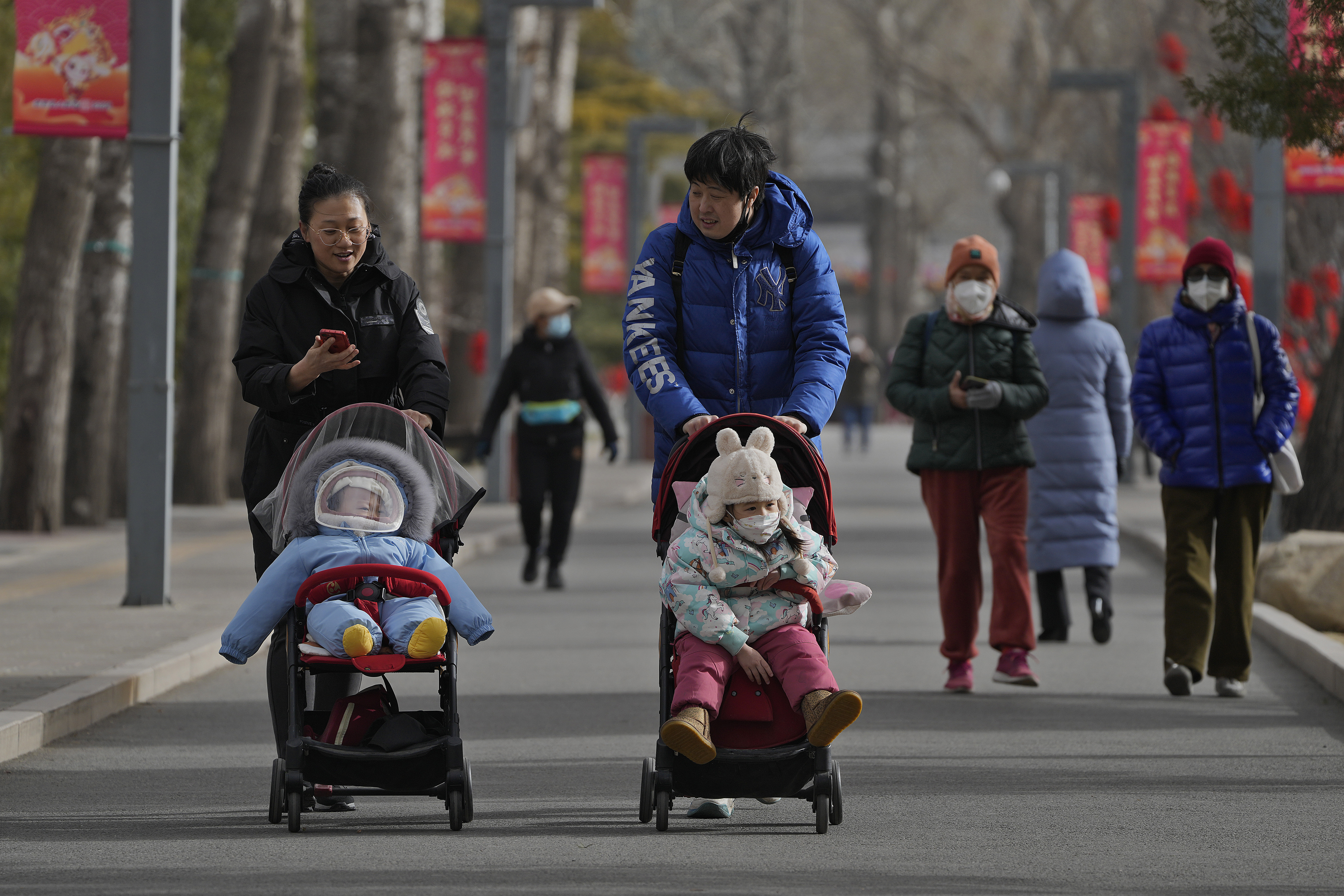 Dos mujeres pasean con niños por un parque en Pekín, China (AP Foto/Andy Wong)