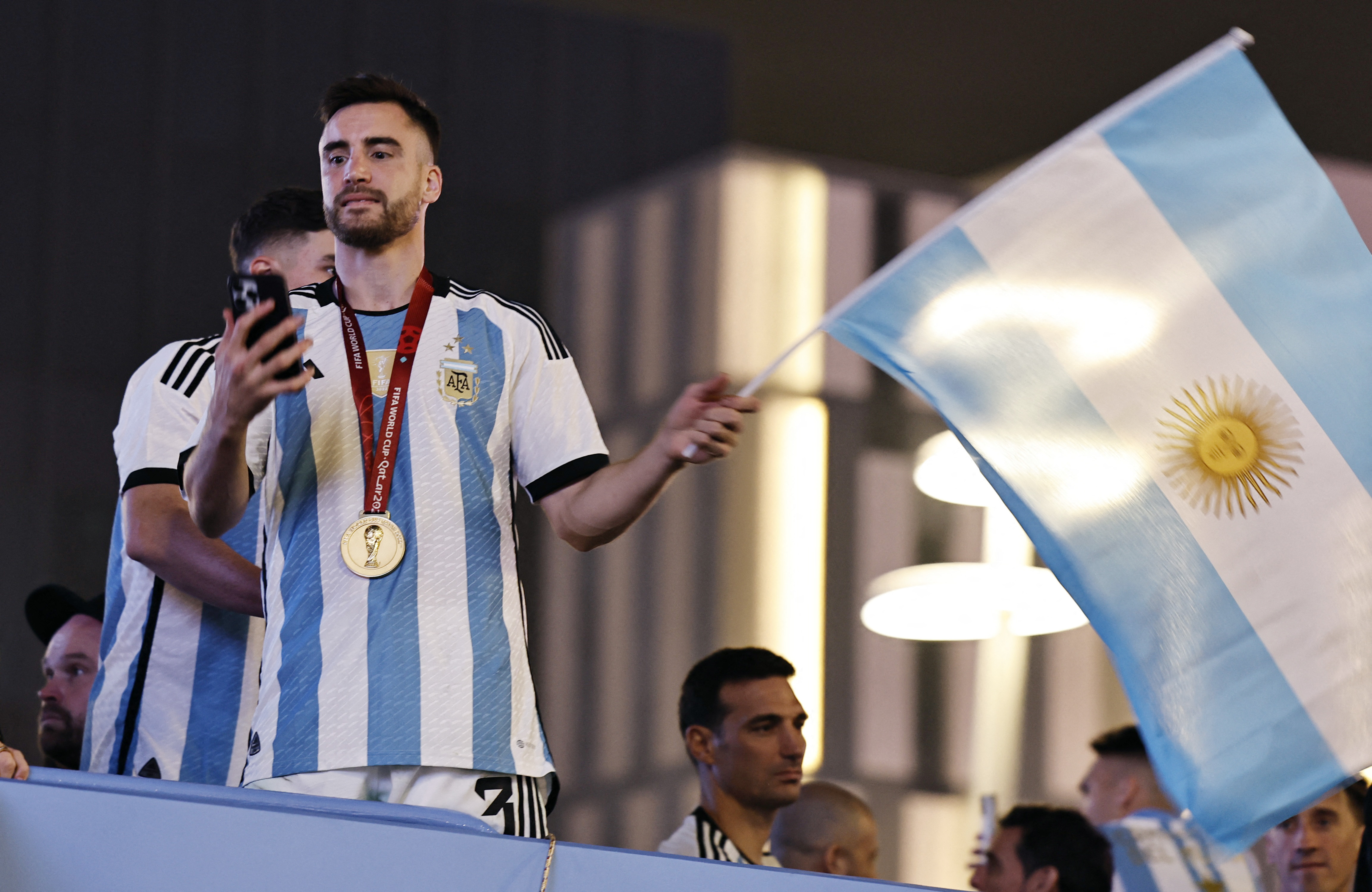 En medio de la celebración sobre el bus, Nicolás Tagliafico controla su celular y agita una bandera argentina. Detrás, el entrenador de la selección nacional, Lionel Scaloni 