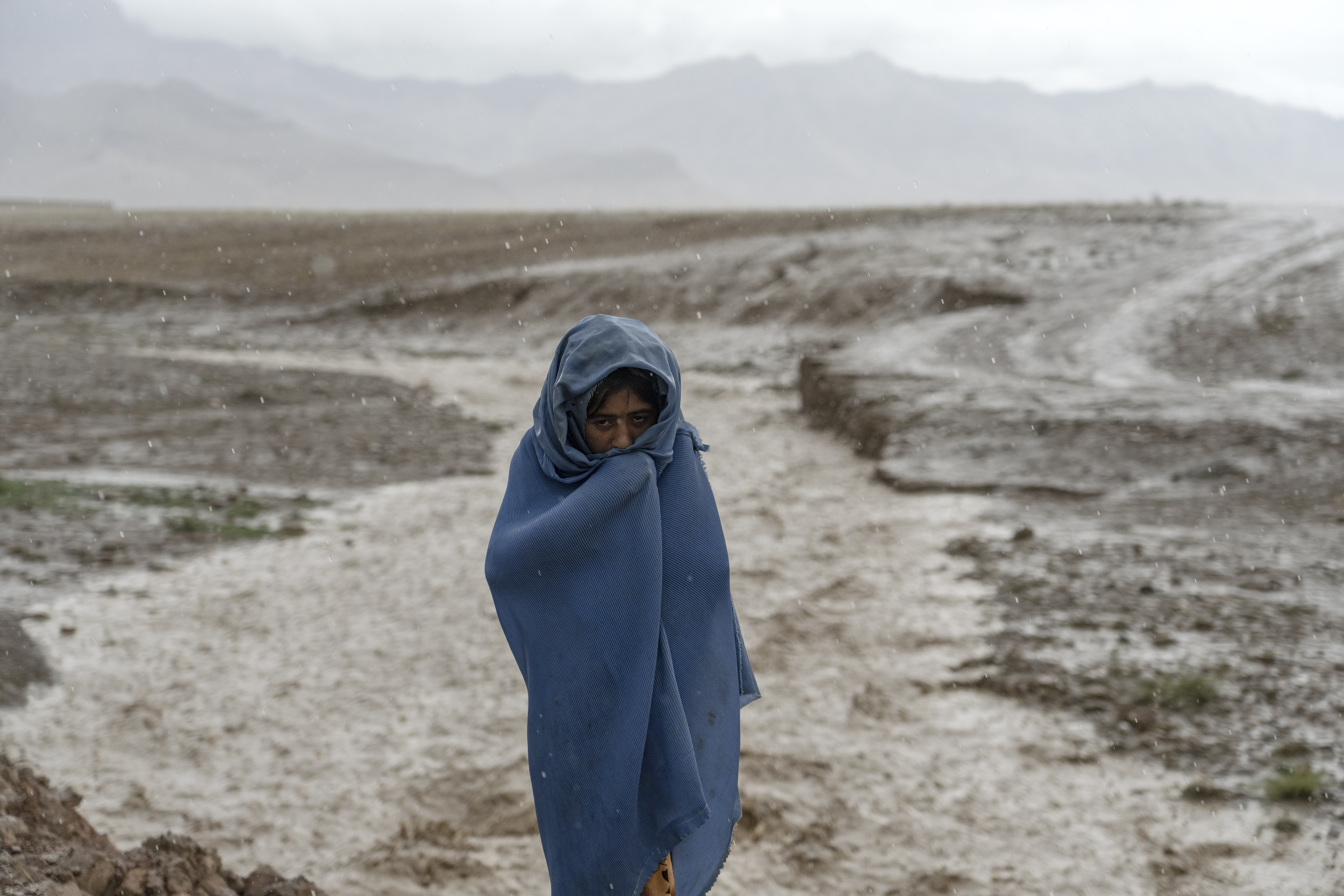 A 9-year-old Afghan girl works in the rain near a brick factory.