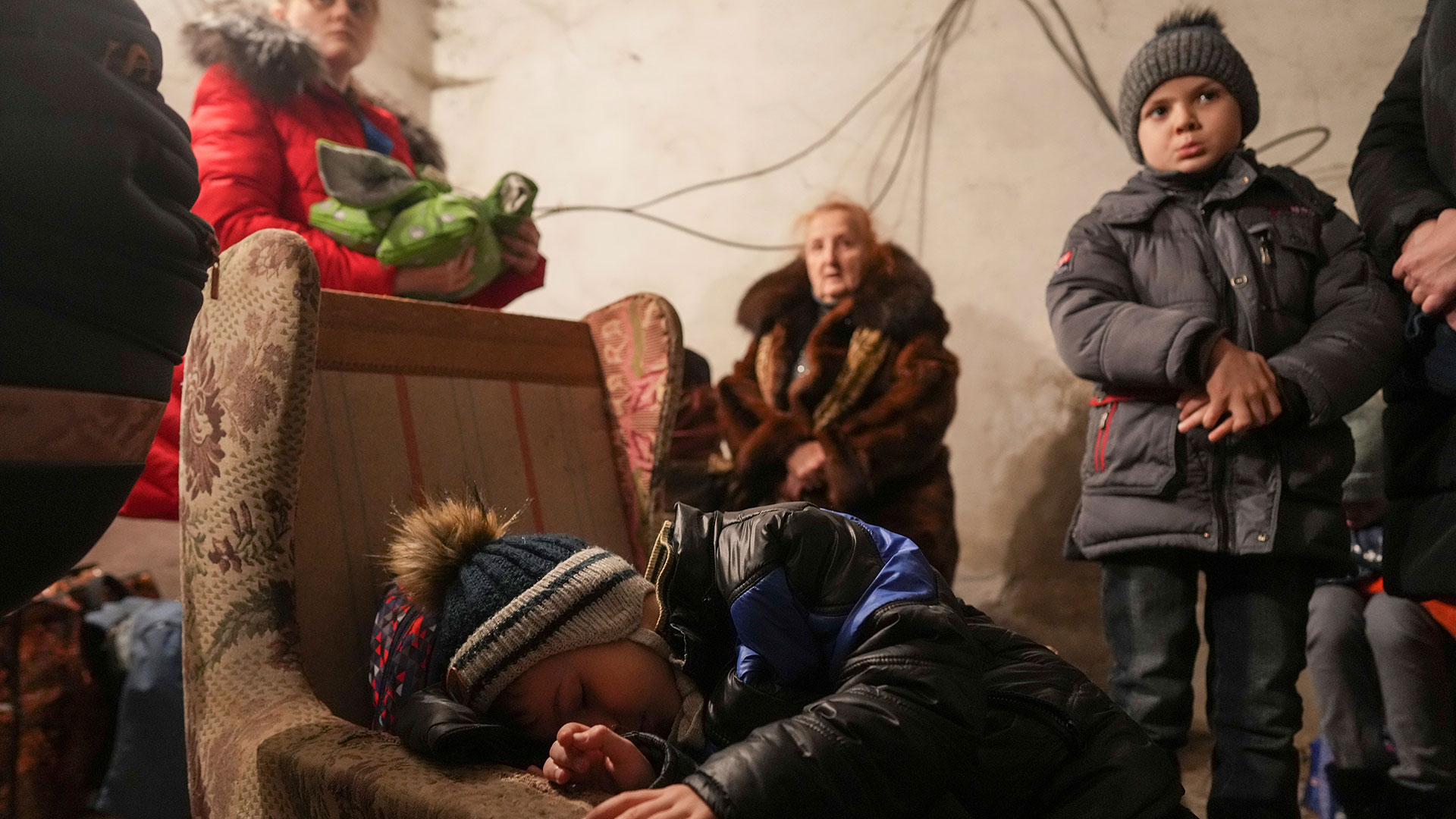 Un niño duerme en un sillón mientras otras personas permanecen alrededor dentro de un refugio durante un bombardeo ruso en Mariupol (AP Foto/Evgeniy Maloletka)