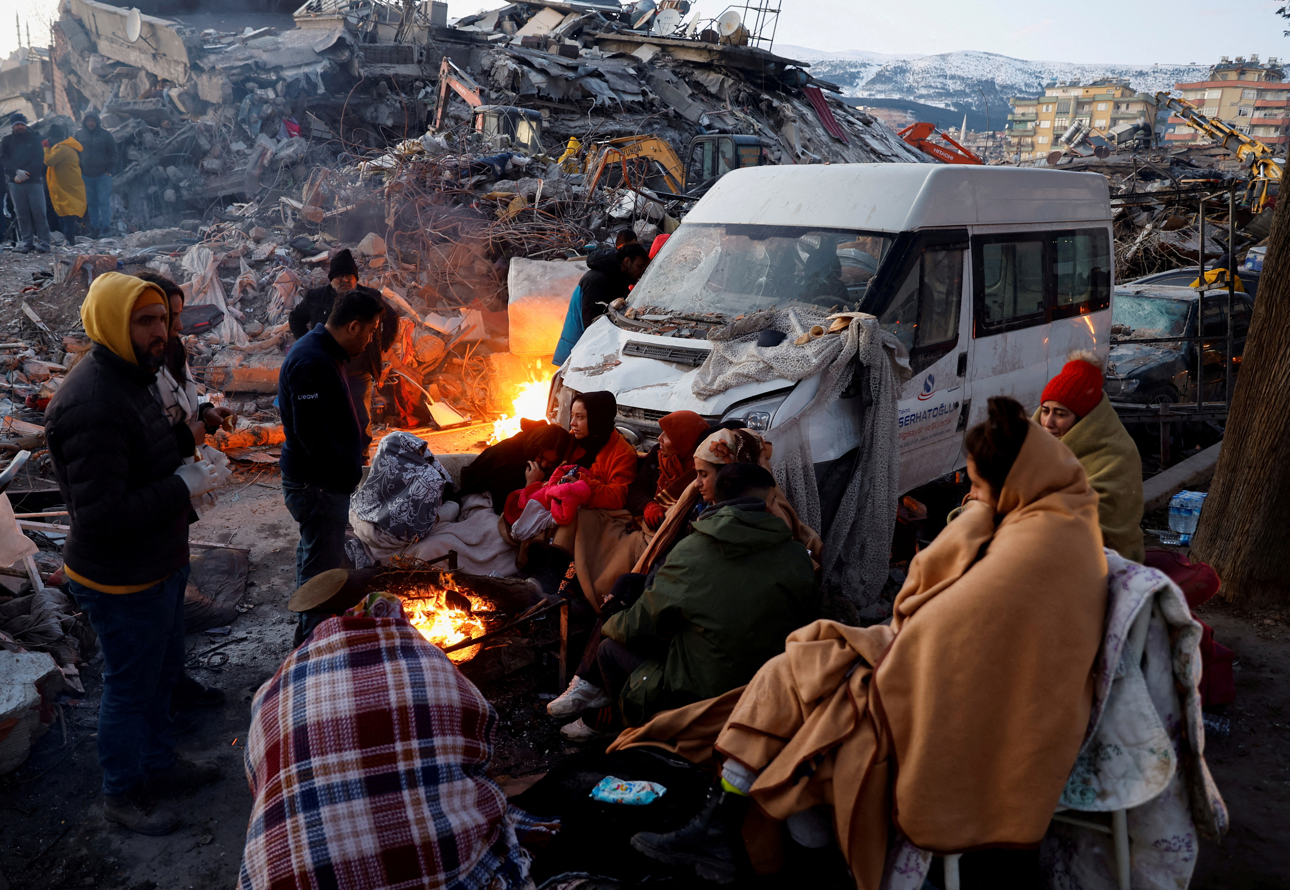 La gente se sienta alrededor de un fuego junto a los escombros y los daños cerca del sitio de un edificio derrumbado en Kahramanmaras, Turquía (REUTERS/Suhaib Salem)