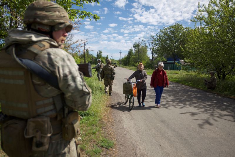 Mujeres caminando por una calle mientras militares ucranianos patrullan la zona (REUTERS/Anna Kudriavtseva)