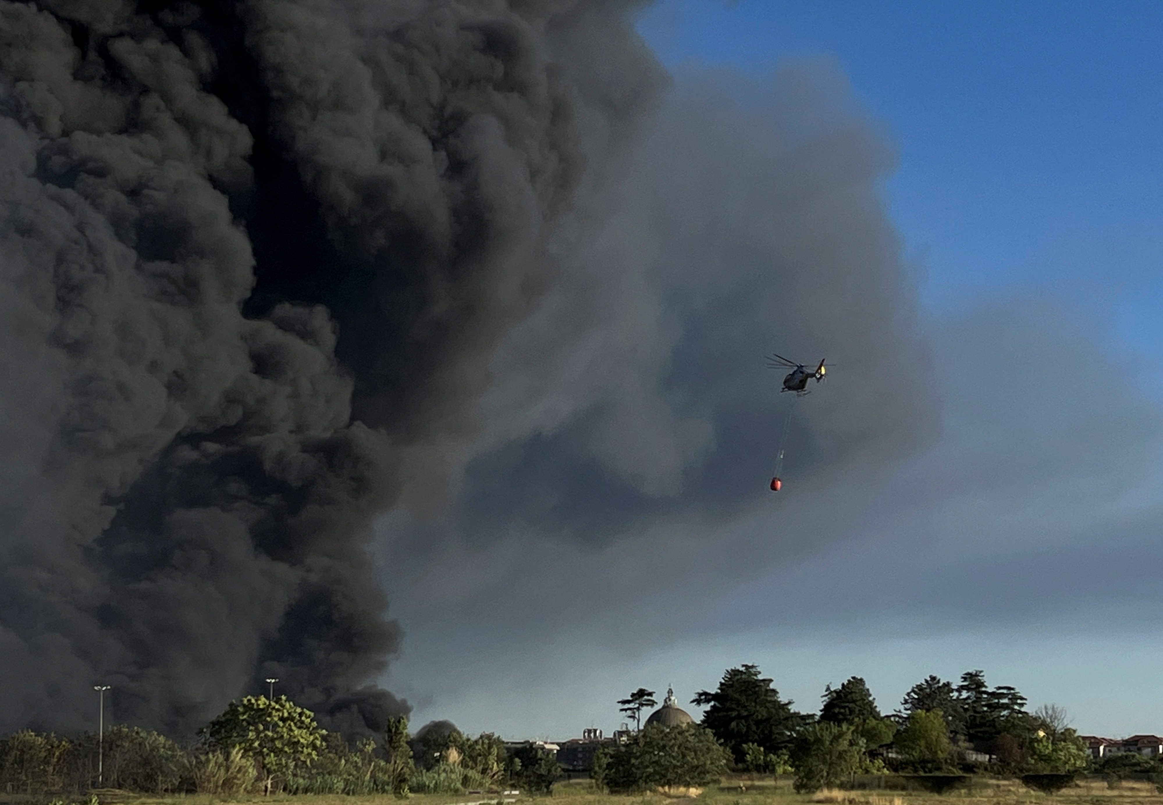 Un helicóptero de bomberos lanza agua para extinguir un incendio mientras el humo se eleva en el Parque Arqueológico de Centocelle en el este de Roma, Italia, este sábado 9 de julio de 2022 (REUTERS/Yara Nardi)