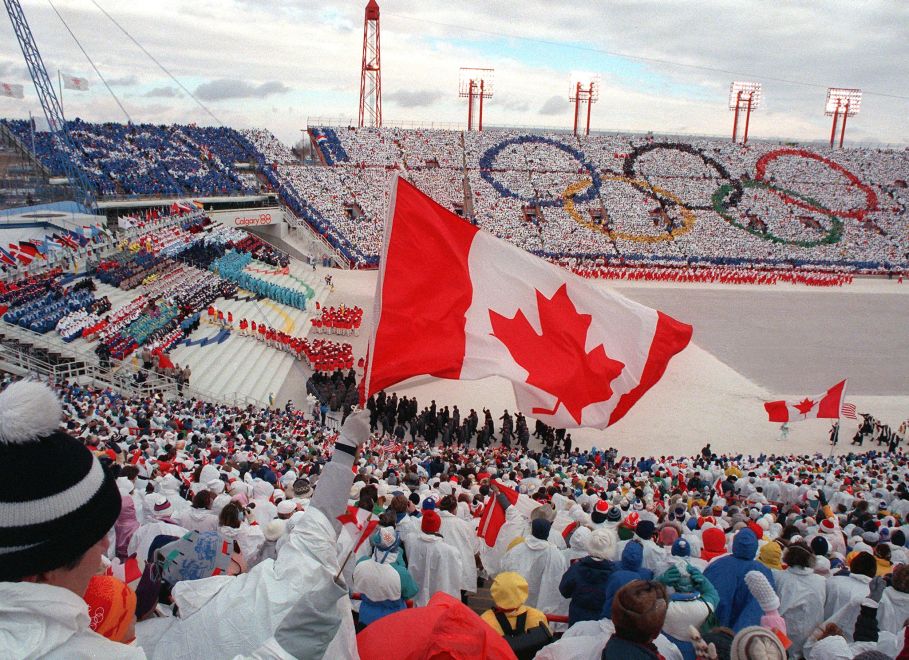 Fans cheer and wave flags as the Canadian delegation (lower right) parades during the opening ceremony of the XVth Winter Olympic Games 13 February 1988 in Calgary.  AFP PHOTO/JONATHAN UTZ (Photo credit should read JONATHAN UTZ/AFP/Getty Images)