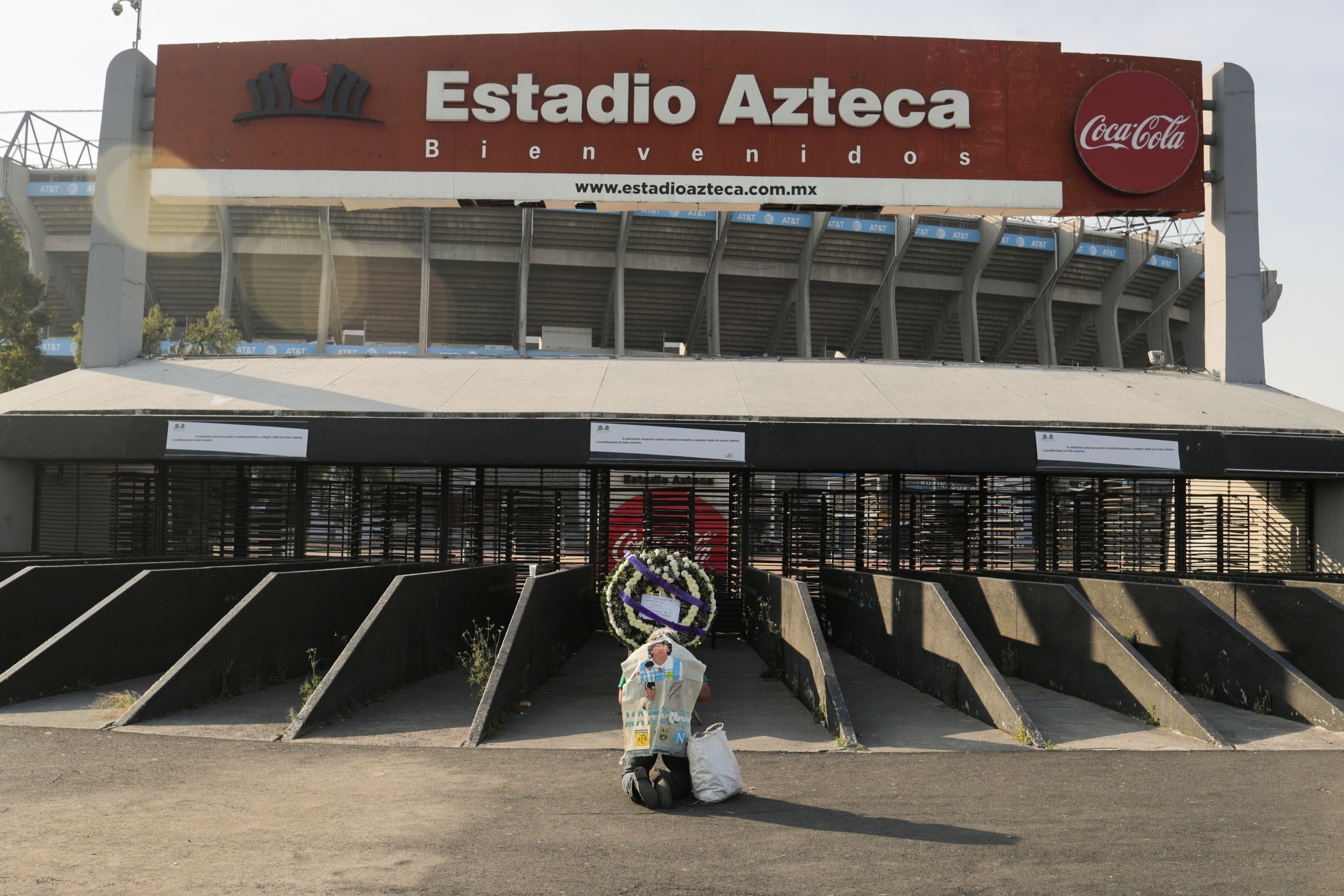 Un fan se arrodilla frente a una ofrenda floral en memoria de Diego Armando Maradona afuera del estadio Azteca, en la Ciudad de México, México, 26 de noviembre de 2020.