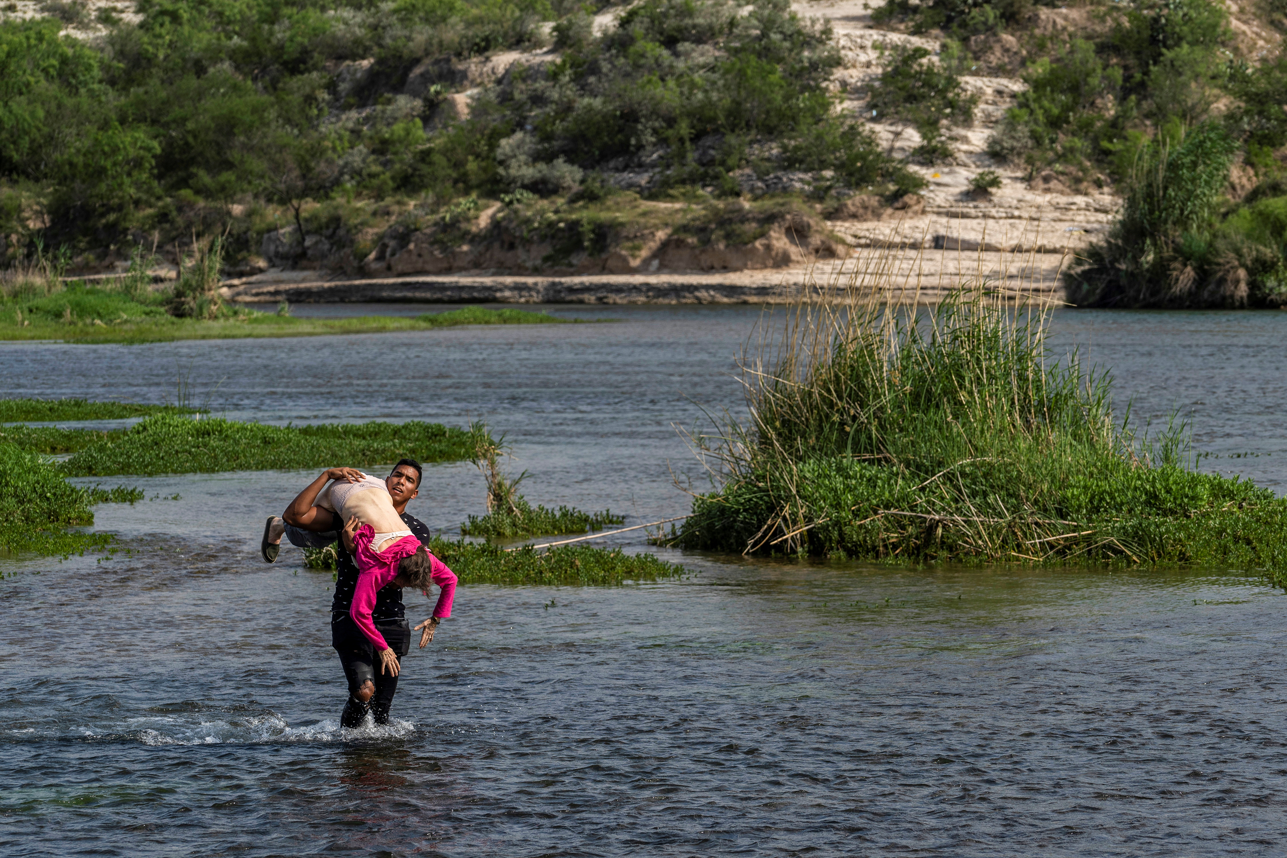 Un joven carga a una abuela a través del río Grande 