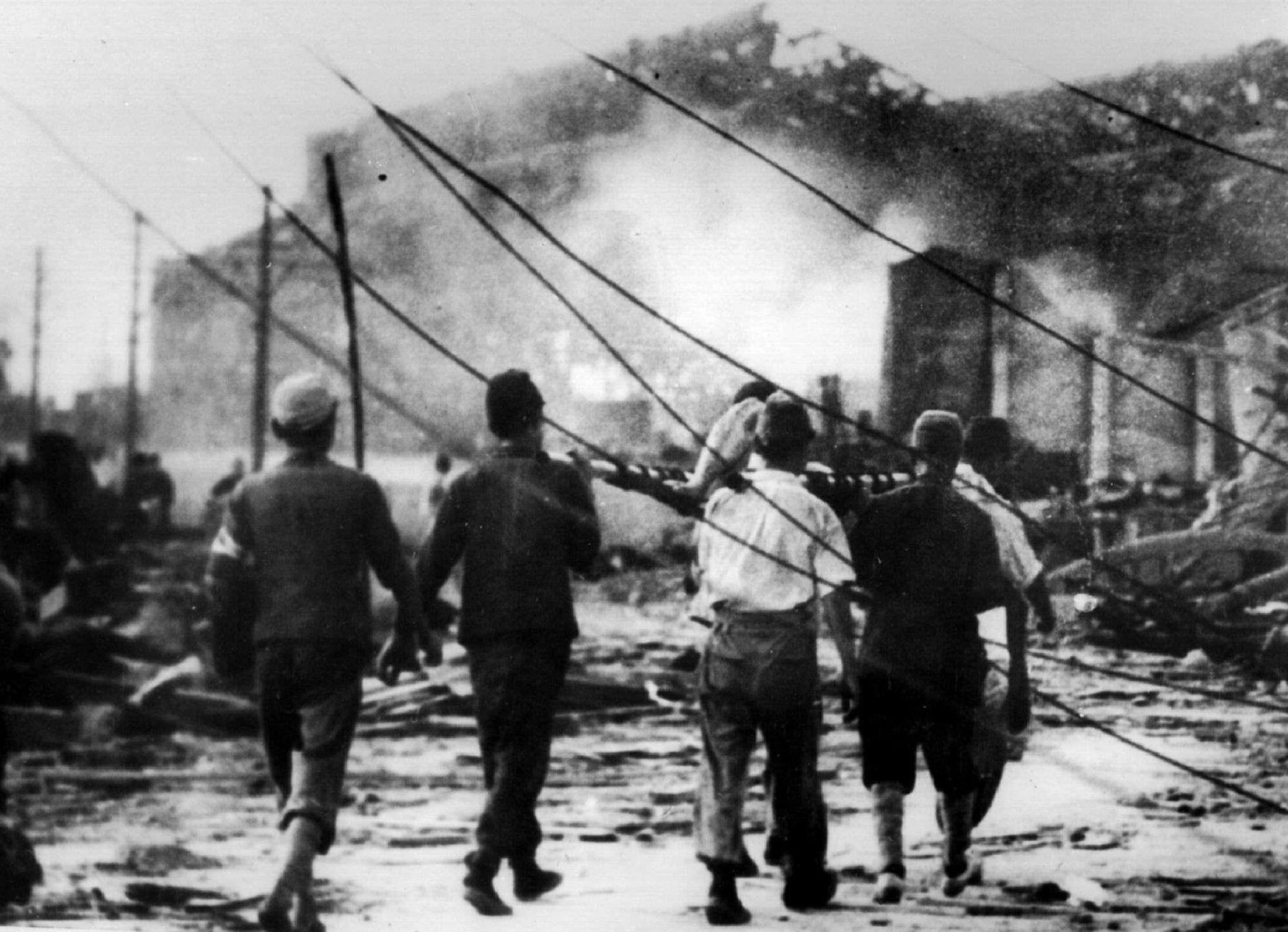 Trabajadores japoneses llevan a una víctima de la bomba atómica lejos de las ruinas humeantes en Hiroshima (REUTERS)