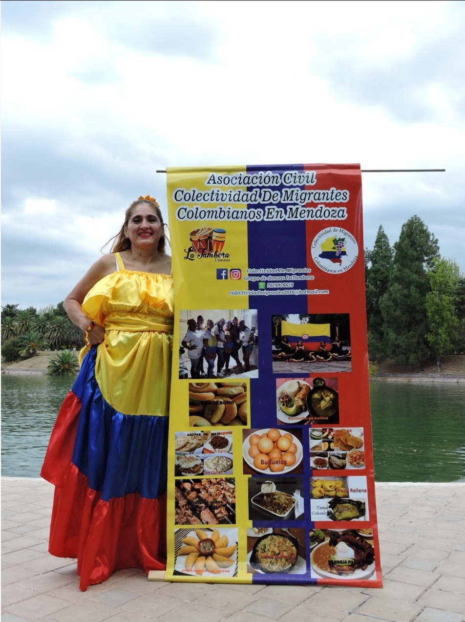 Yamilet vestida con los colores de su país, con el estandarte de la Asociación Civil Migrantes Colombianos en Mendoza con las exquisiteces que preparan en el emprendimiento gastronómico que llevan adelante