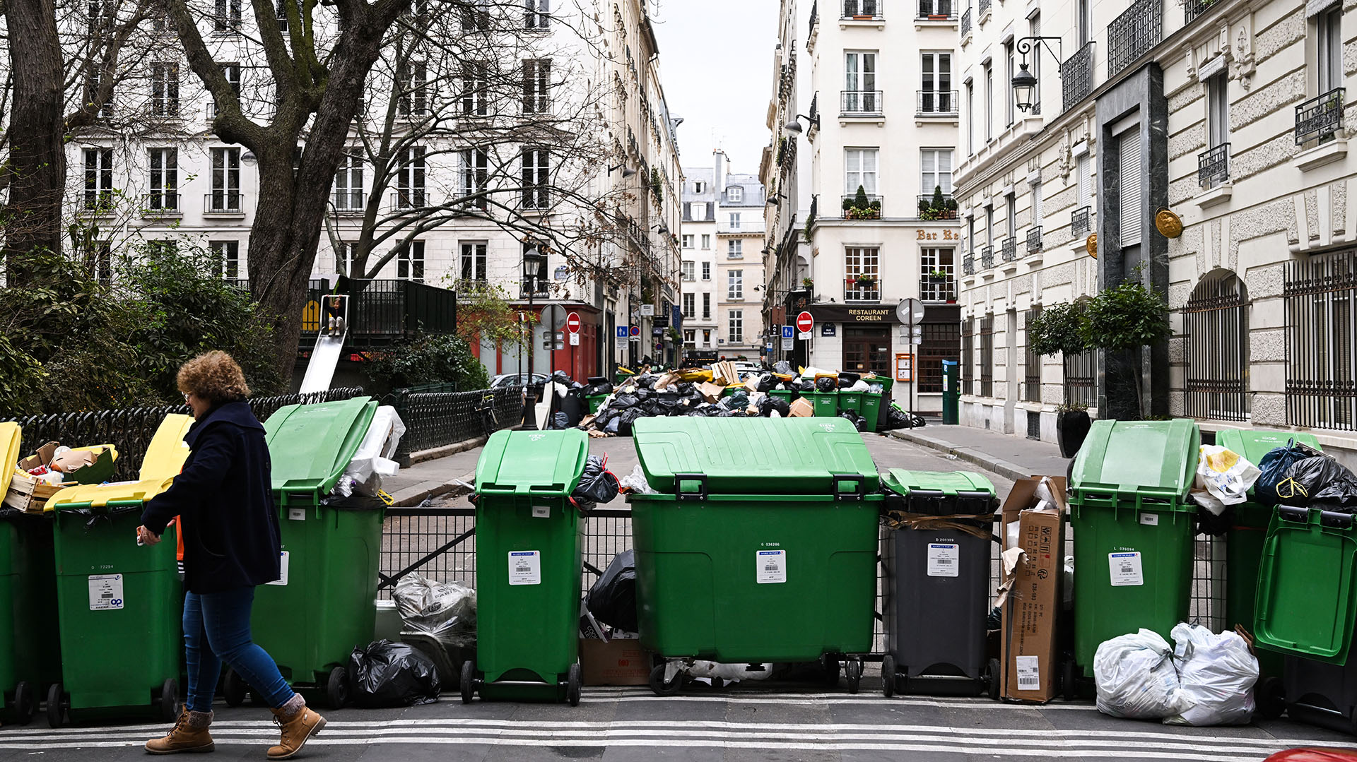 Un peatón pasa junto a contenedores de basura doméstica en una calle de París, el 12 de marzo de 2023. (Foto de Stefano RELLANDINI / AFP)
