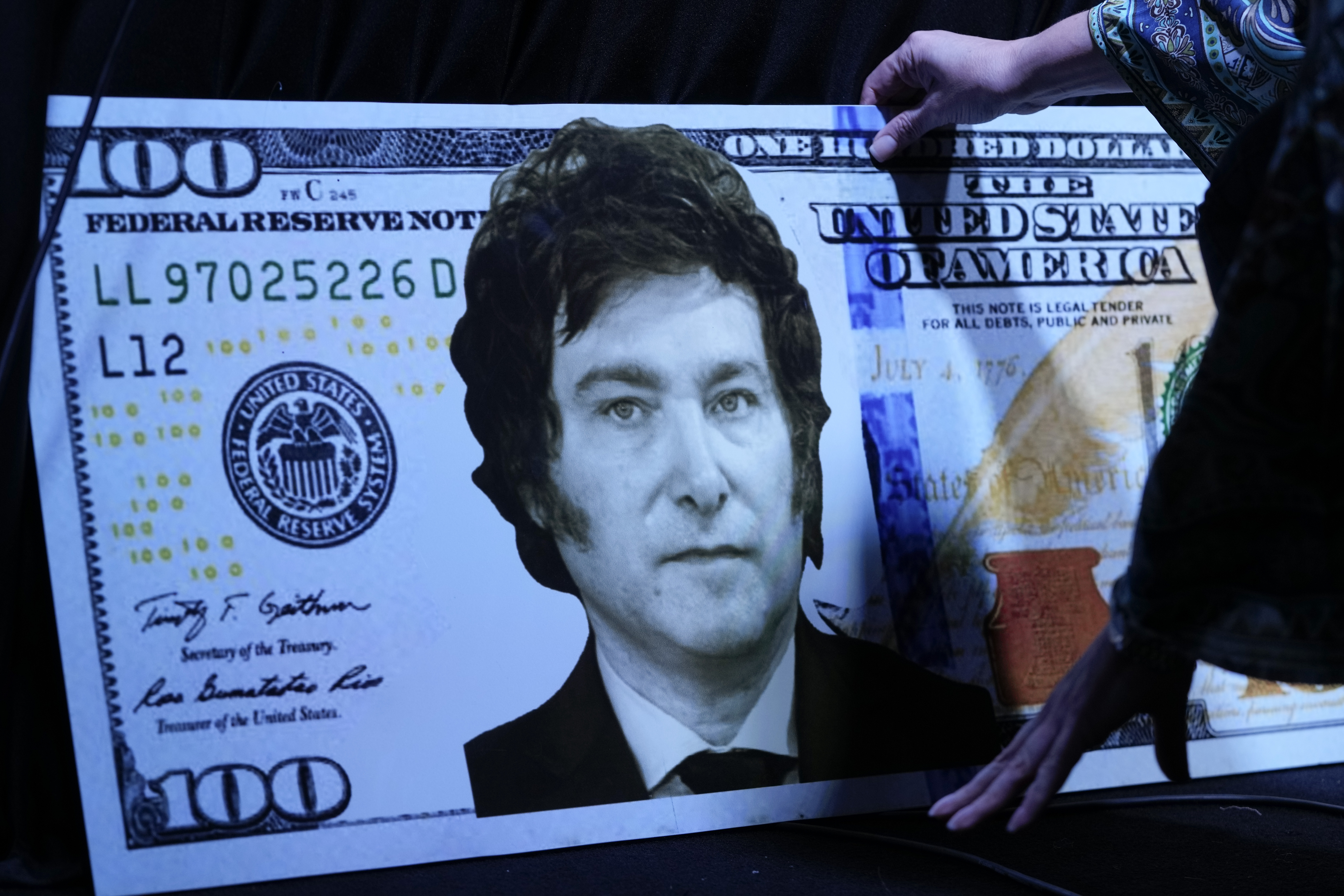 La hermana del candidato presidencial argentino Javier Milei, Karina Milei, coloca una foto de su hermano en un billete de cartón de 100 dólares antes del inicio de la presentación del libro de su hermano "El fin de la inflación" en la Feria del Libro de Buenos Aires, Argentina, el domingo 14 de mayo de 2023. (AP)