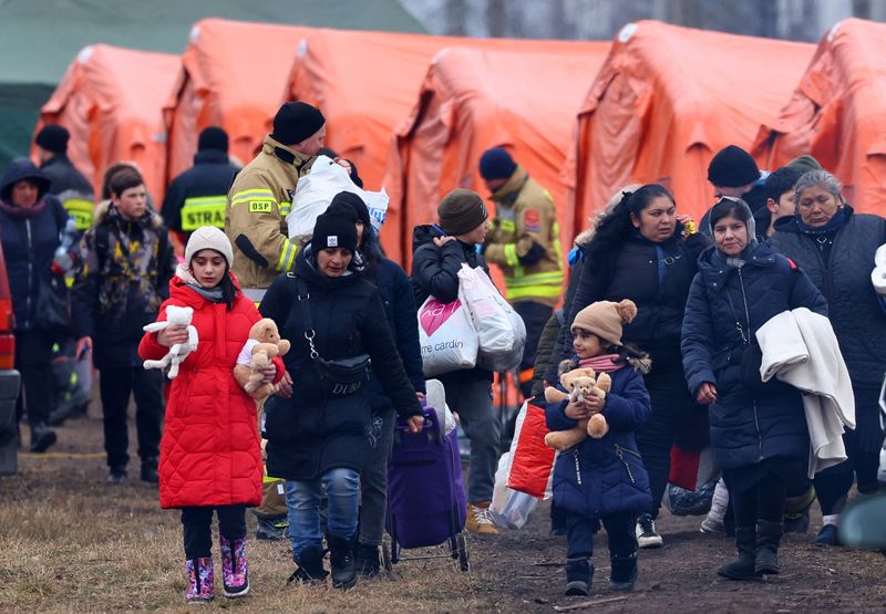 Personas y niños esperan cerca de tiendas de campaña después de cruzar la frontera de Ucrania a Polonia