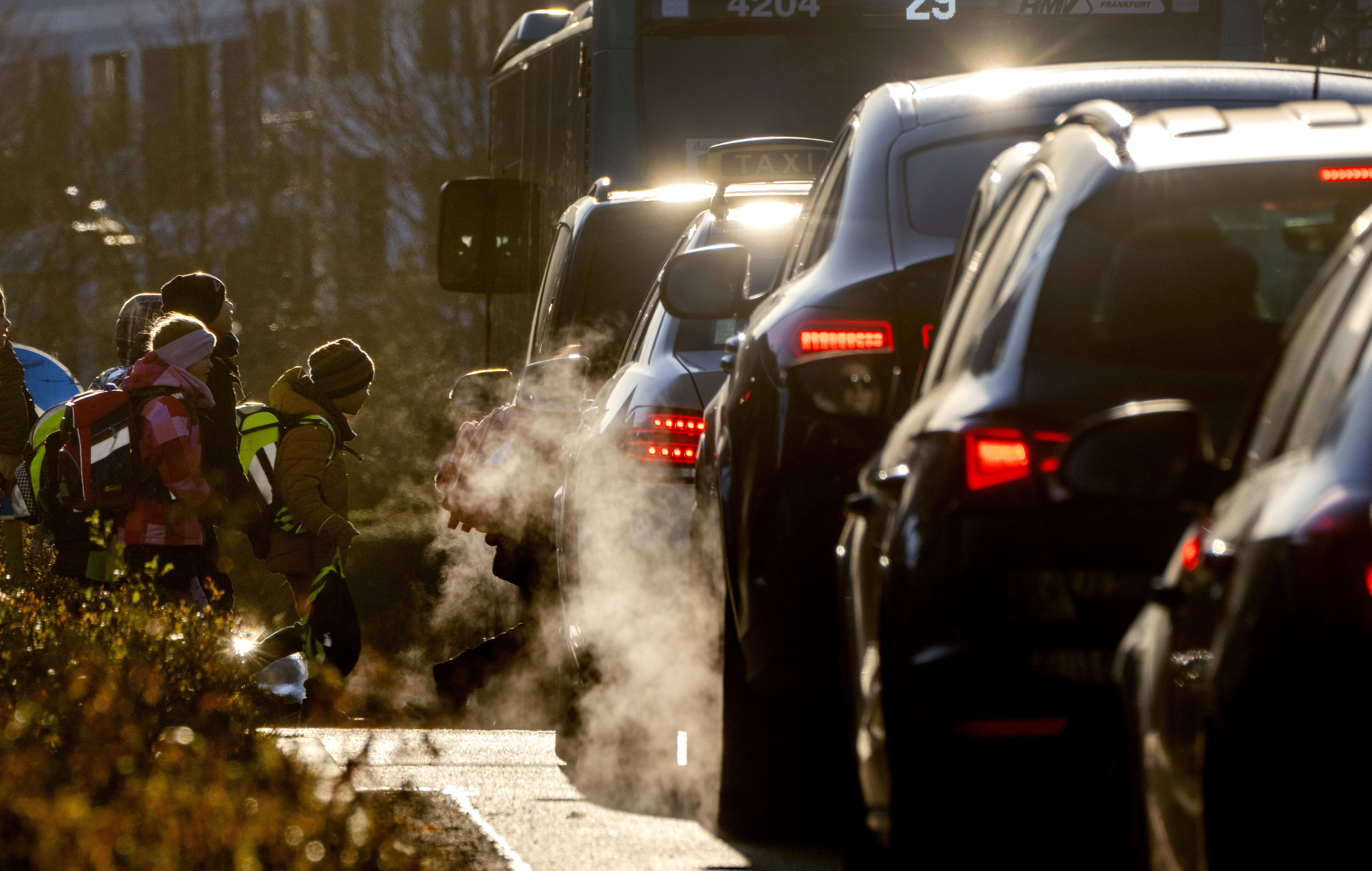 Automóviles emiten gases de escape mientras niños caminan a una escuela de Fráncfort, Alemania, el lunes 27 de febrero de 2023. (AP Foto/Michael Probst)