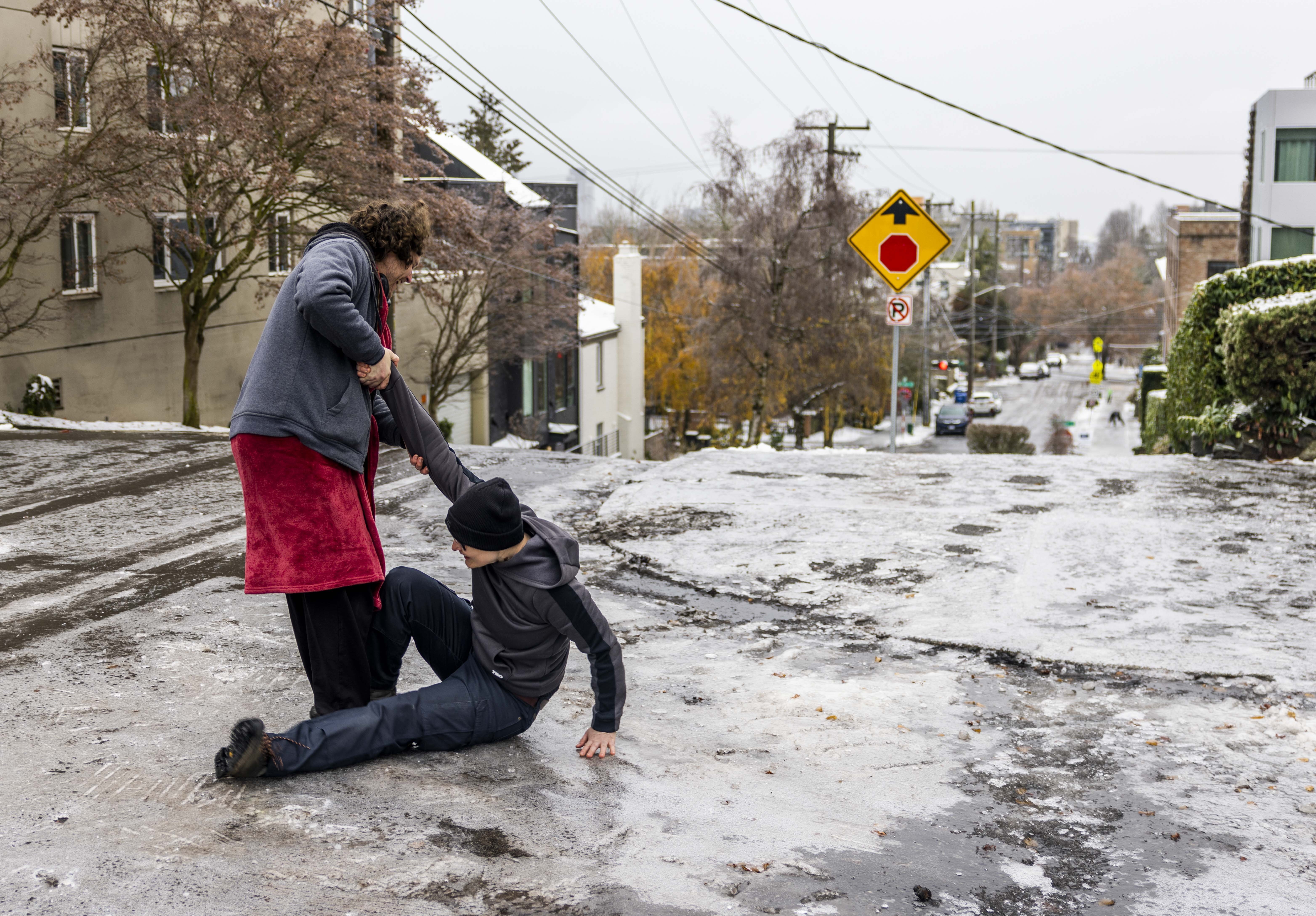 Garrett Fuller, a la izquierda, ayuda a su amigo Robin Jacobs a levantarse después de resbalar al suelo helado en Capitol Hill, el viernes en Seattle. 