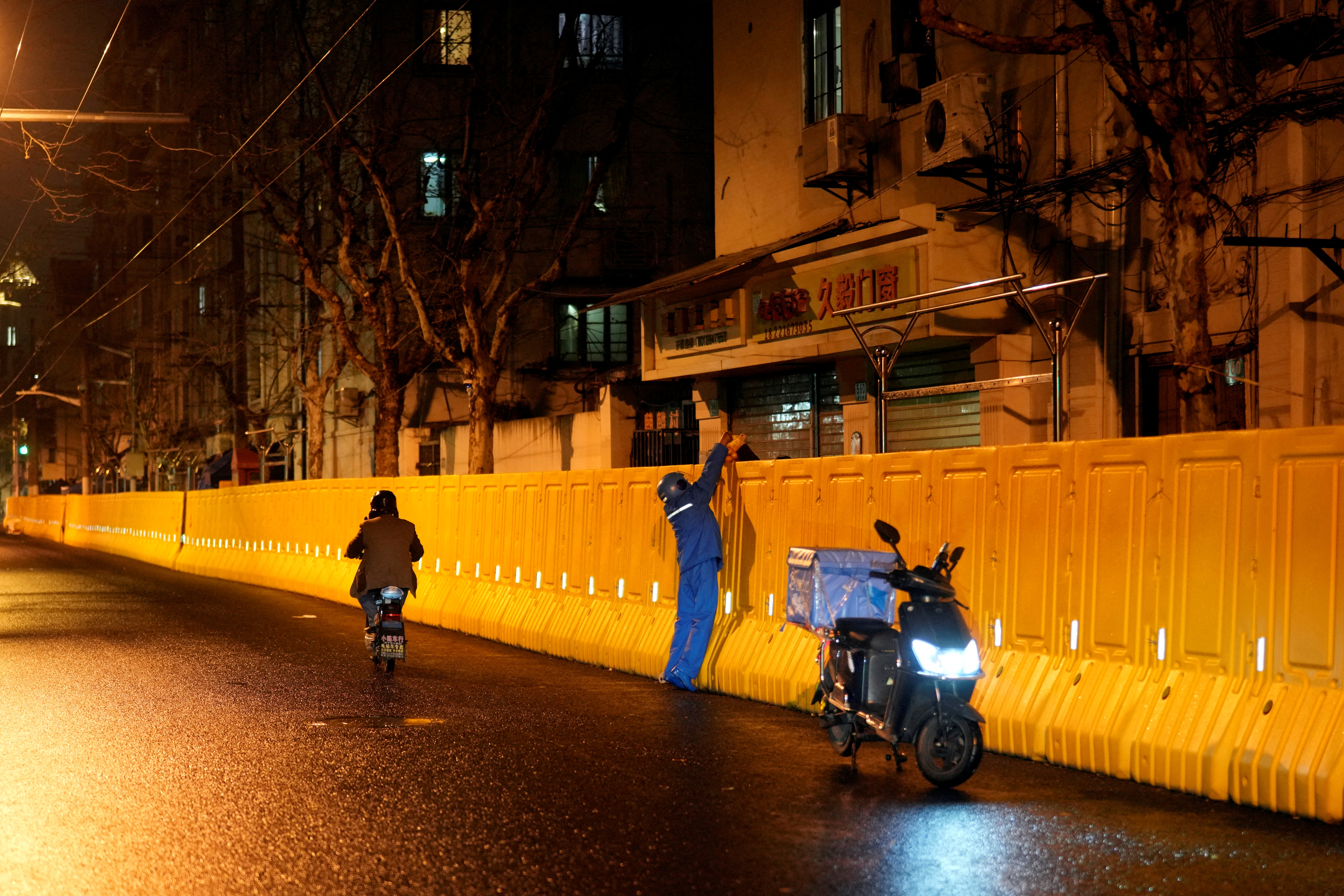 Un repartidor entrega un pedido a un residente detrás de las barreras que sellan una zona de Shanghai (REUTERS/Aly Song)