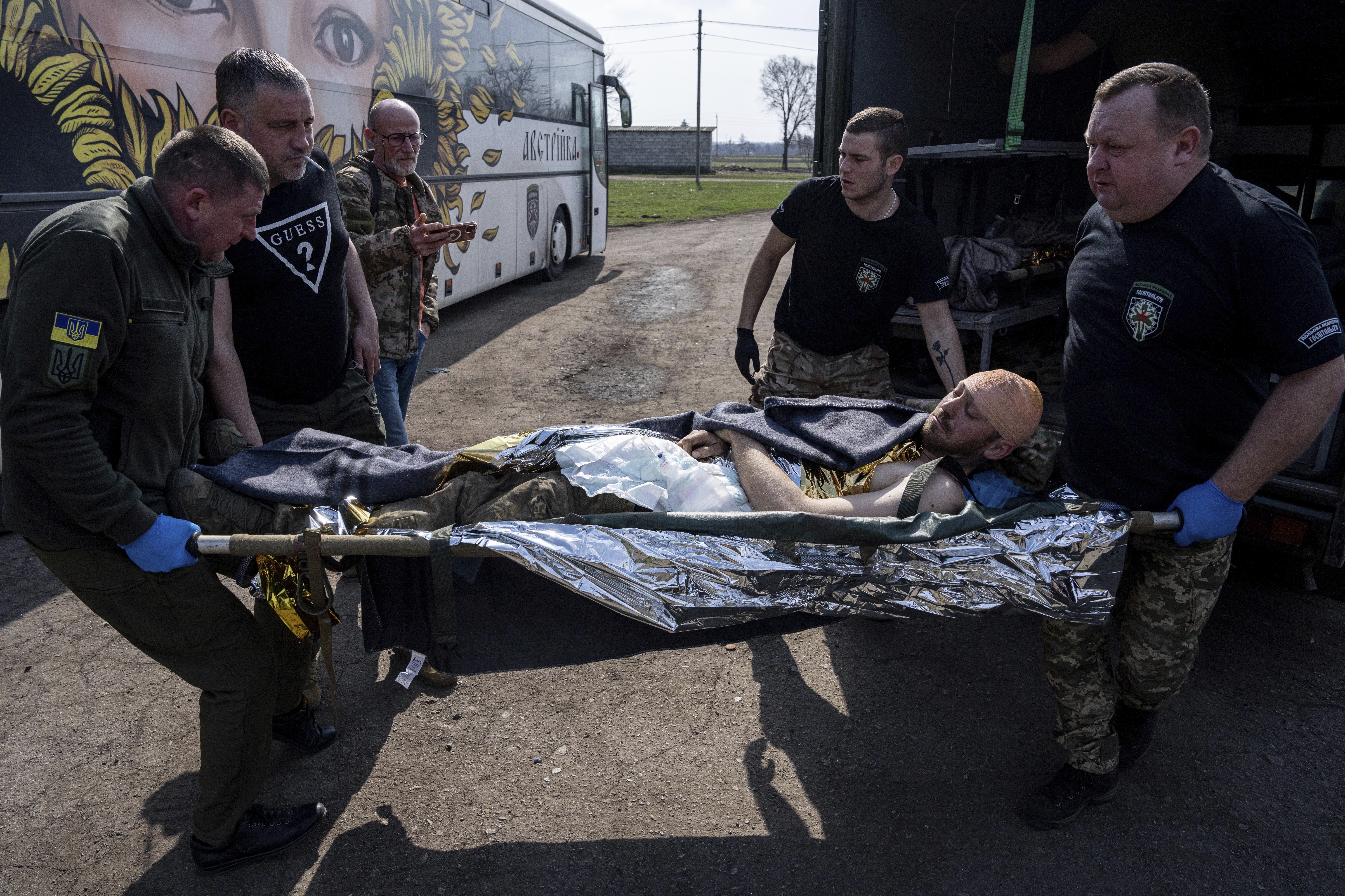 Voluntarios de la organización paramédica Hospitallers llevan a un soldado ucraniano herido a un autobús médico especial durante una evacuación en la región de Donetsk, Ucrania, el miércoles 22 de marzo de 2023. (AP Foto/Evgeniy Maloletka)